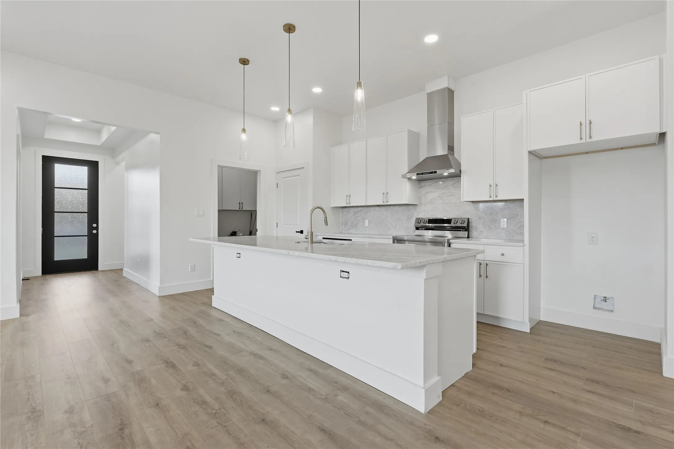 Kitchen featuring a center island with a light-toned countertop, stainless steel appliances, a range hood, and white cabinetry