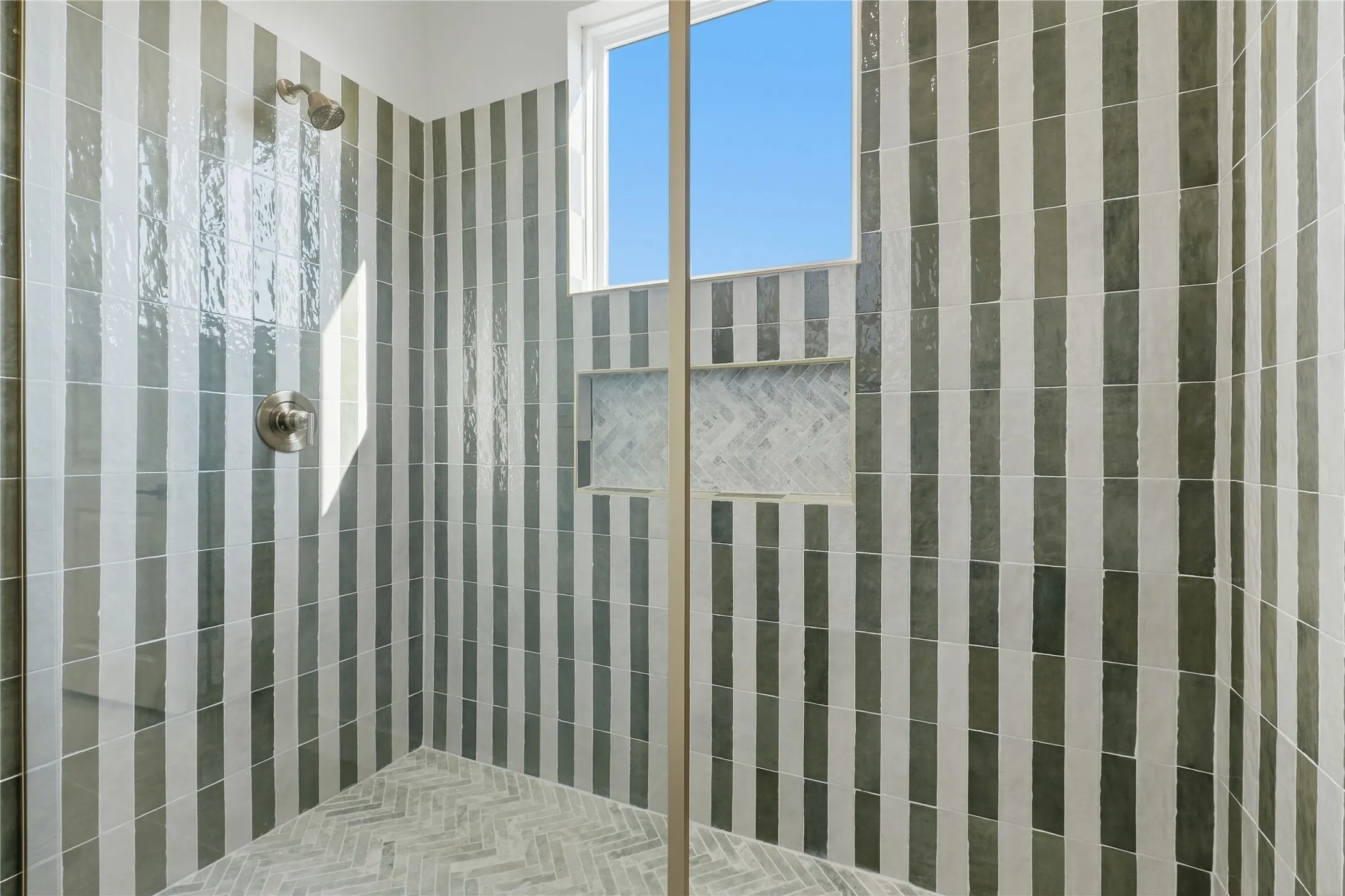 Shower featuring striped wall tiling, recessed shelving with herringbone tile, a window, and brushed nickel fixtures