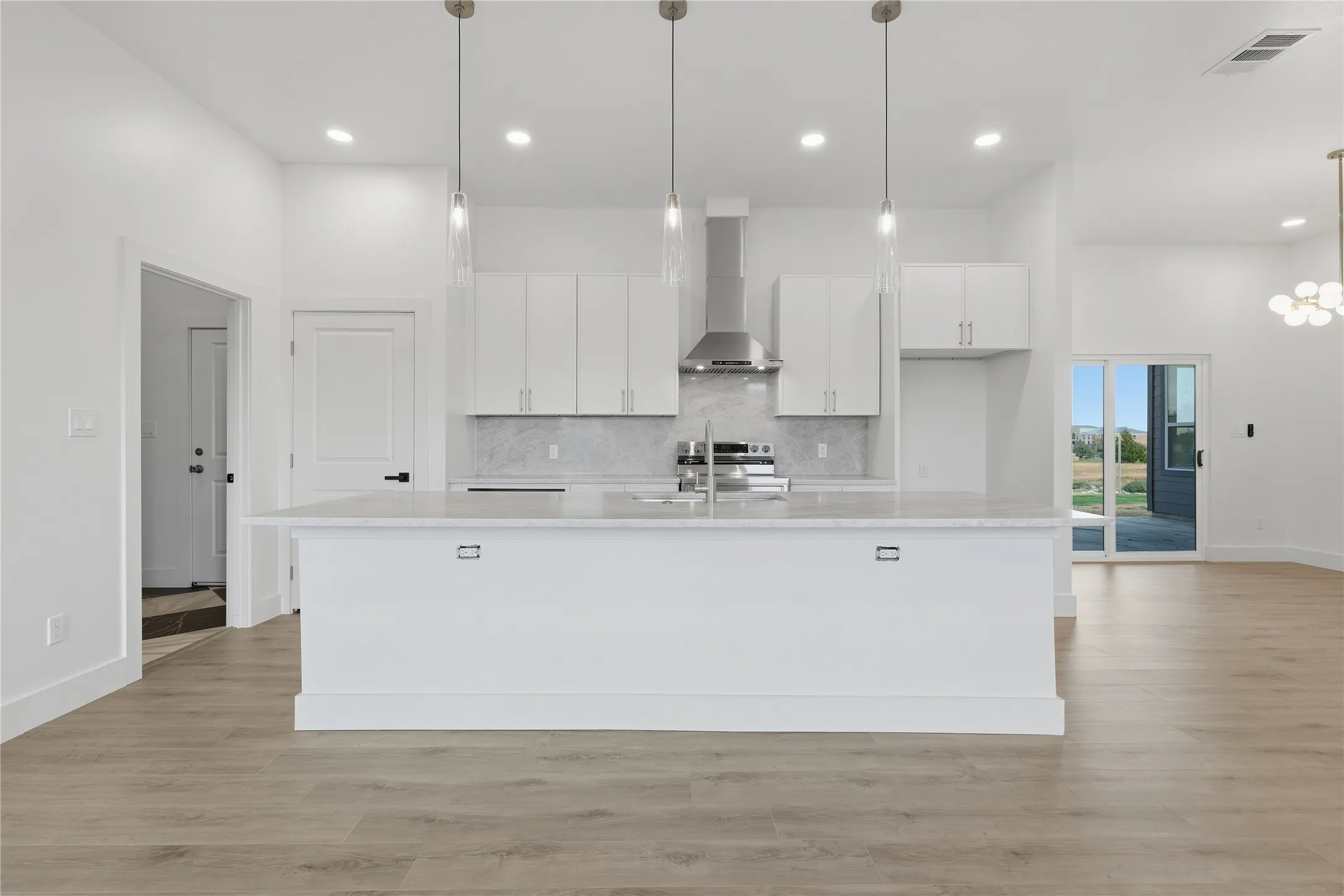 Open-concept kitchen featuring white cabinetry, a large center island with a light-toned countertop, stainless steel appliances, and pendant lighting