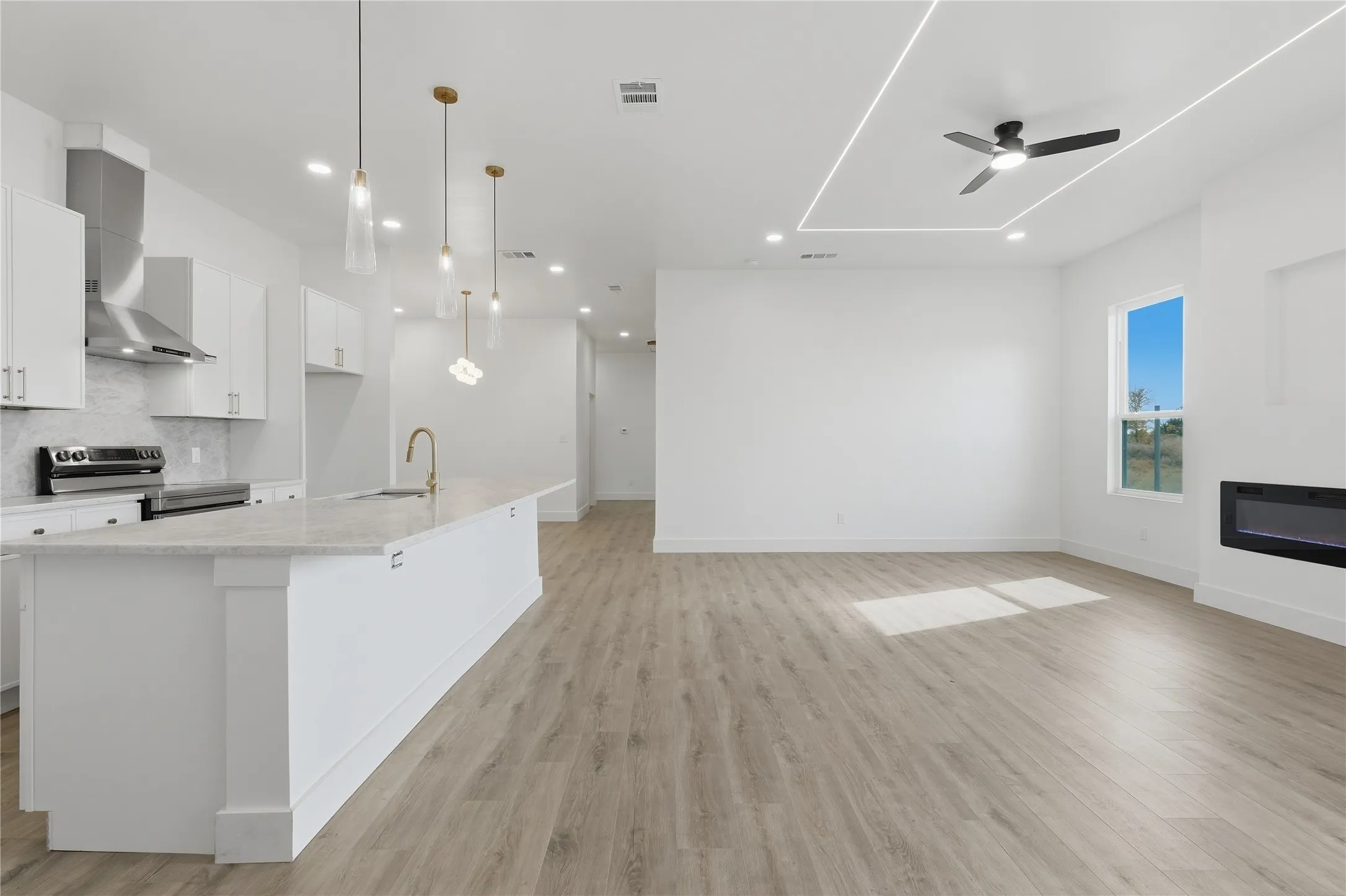 Open-concept living space with wood-finish flooring, a contemporary fireplace, and a kitchen island with pendant lighting