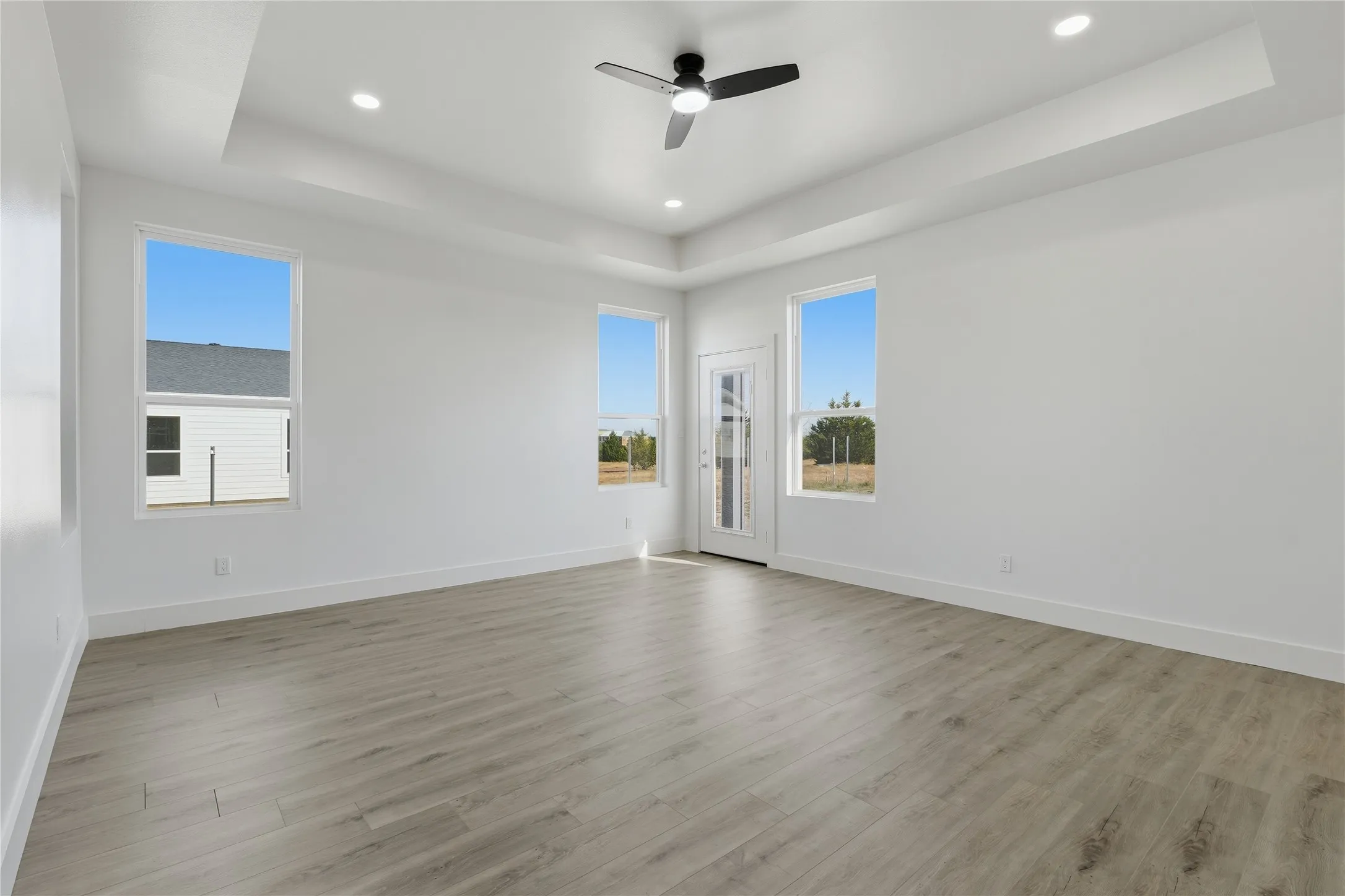 Tray ceiling with recessed lighting, wood-finish flooring, ceiling fan, multiple windows, and a glass-paned door