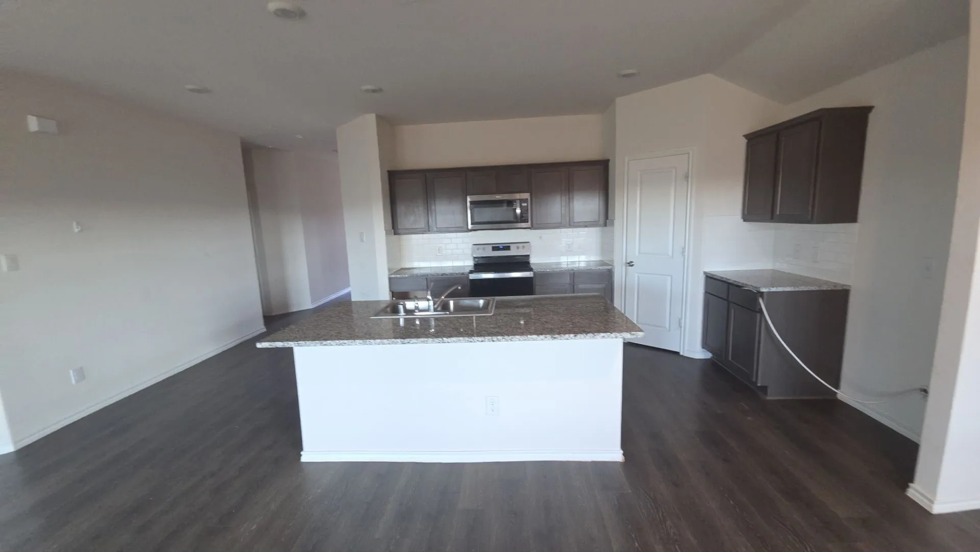 Kitchen featuring a central island with a sink, recessed lighting, wood-finish flooring, dark cabinetry, and white subway tile backsplash