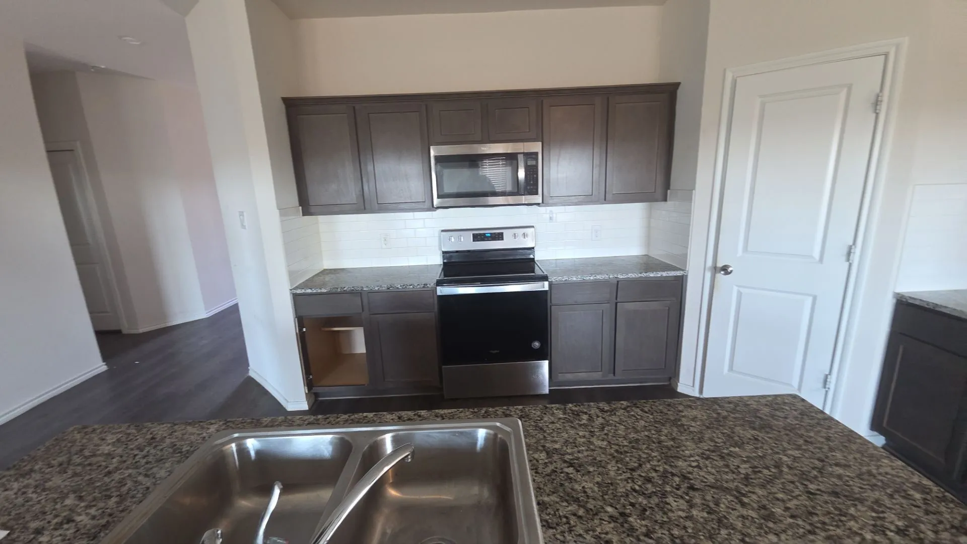 Kitchen featuring dark wood-finish cabinetry, granite-style countertops, stainless steel appliances, and a white subway tile backsplash