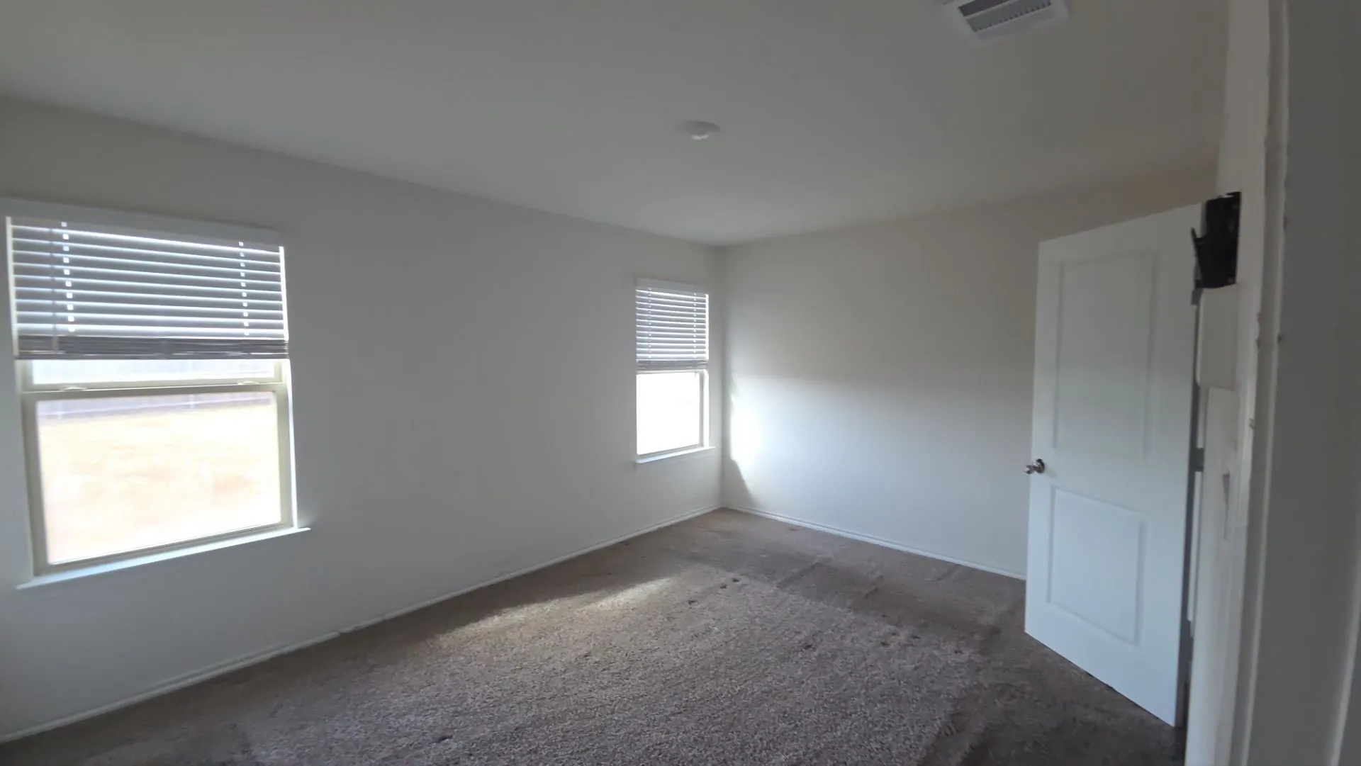 Soft gray carpeting, two windows with blinds, white paneled door, and recessed lighting