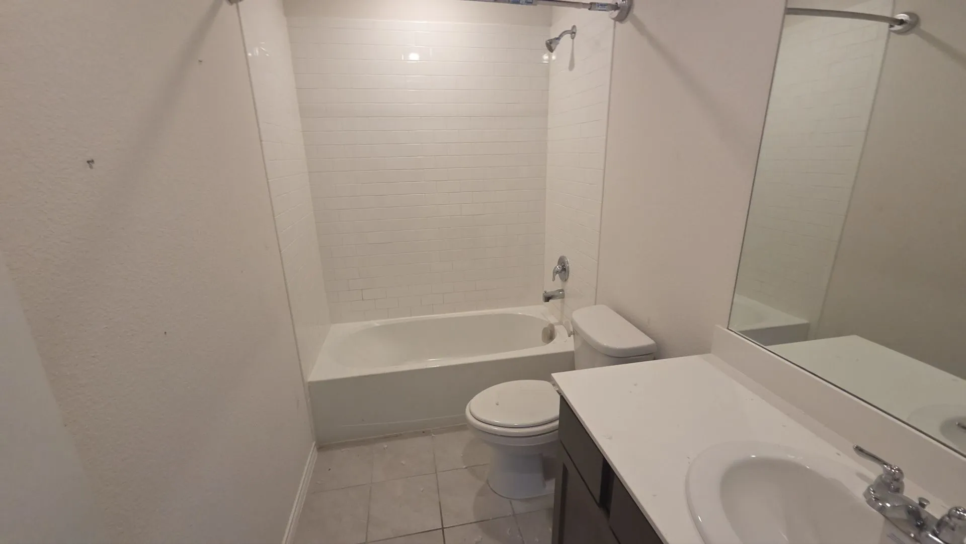 Bathroom featuring a white subway tile shower surround, a full-size bathtub, a dark wood-finish vanity with a white countertop, and tiled flooring