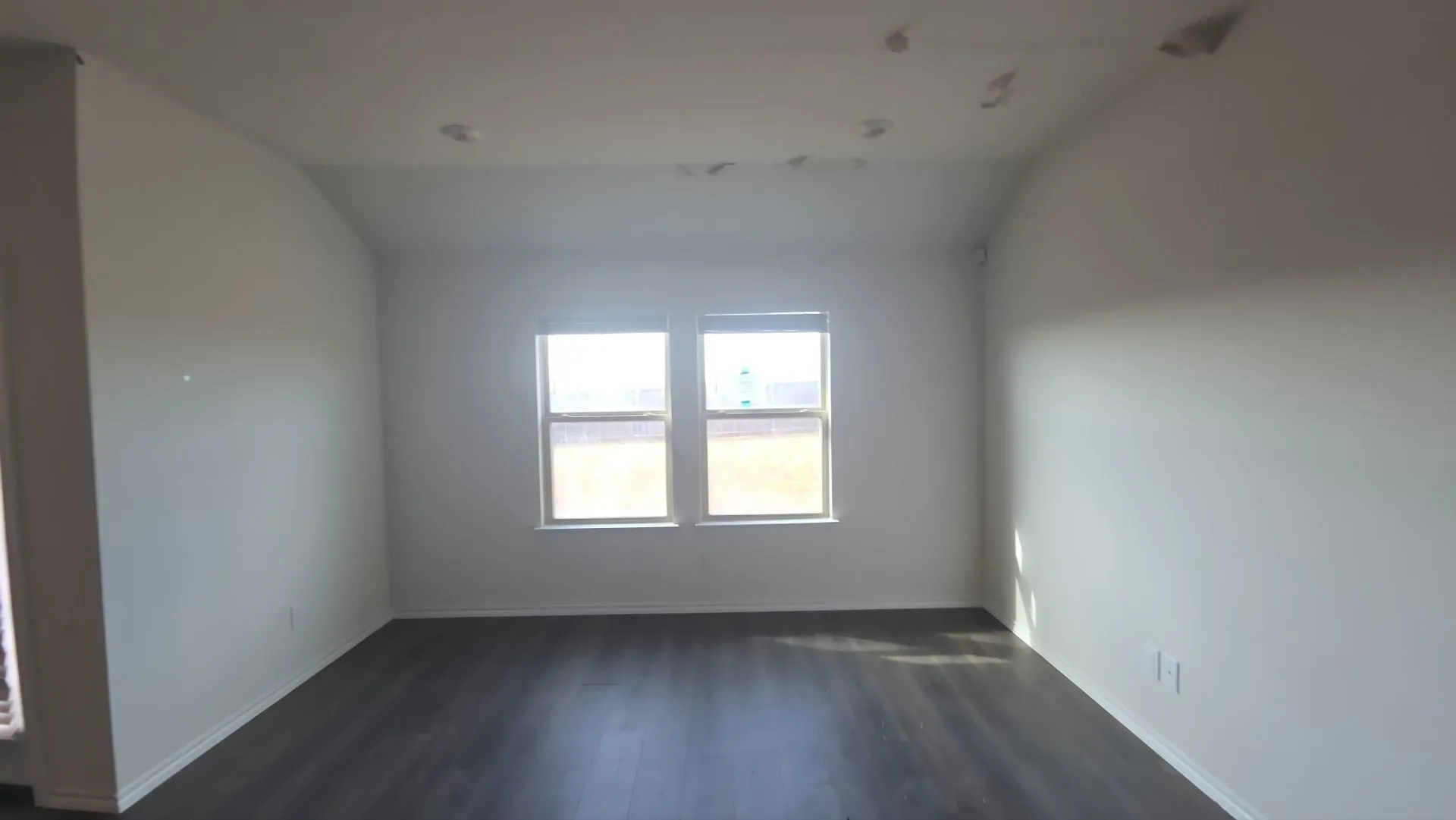 Vaulted ceiling with recessed lighting, two windows, wood-finish flooring, and crisp white walls