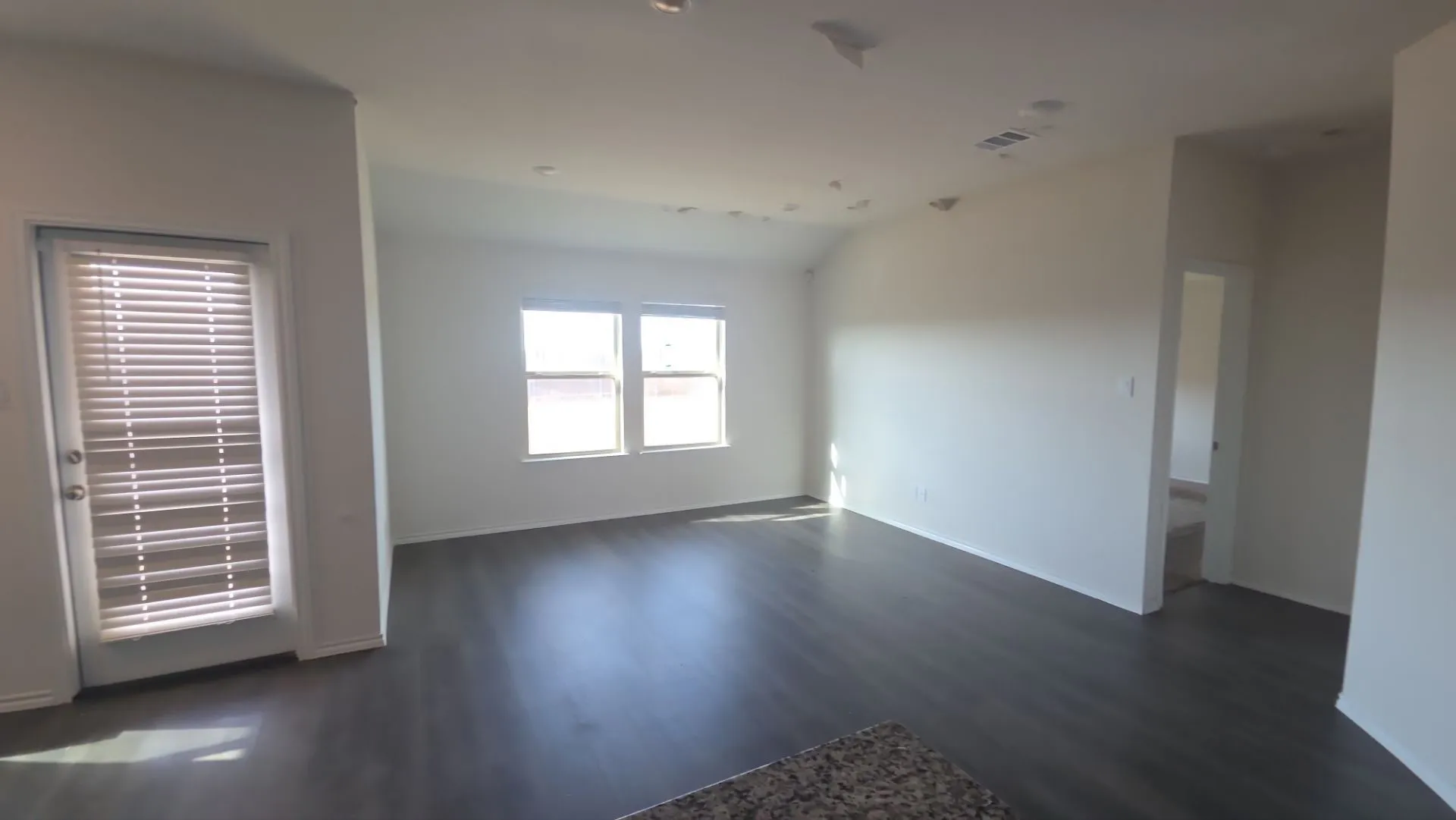 Spacious room featuring vaulted ceilings, dark wood-finish flooring, recessed lighting, and a white paneled door with horizontal blinds