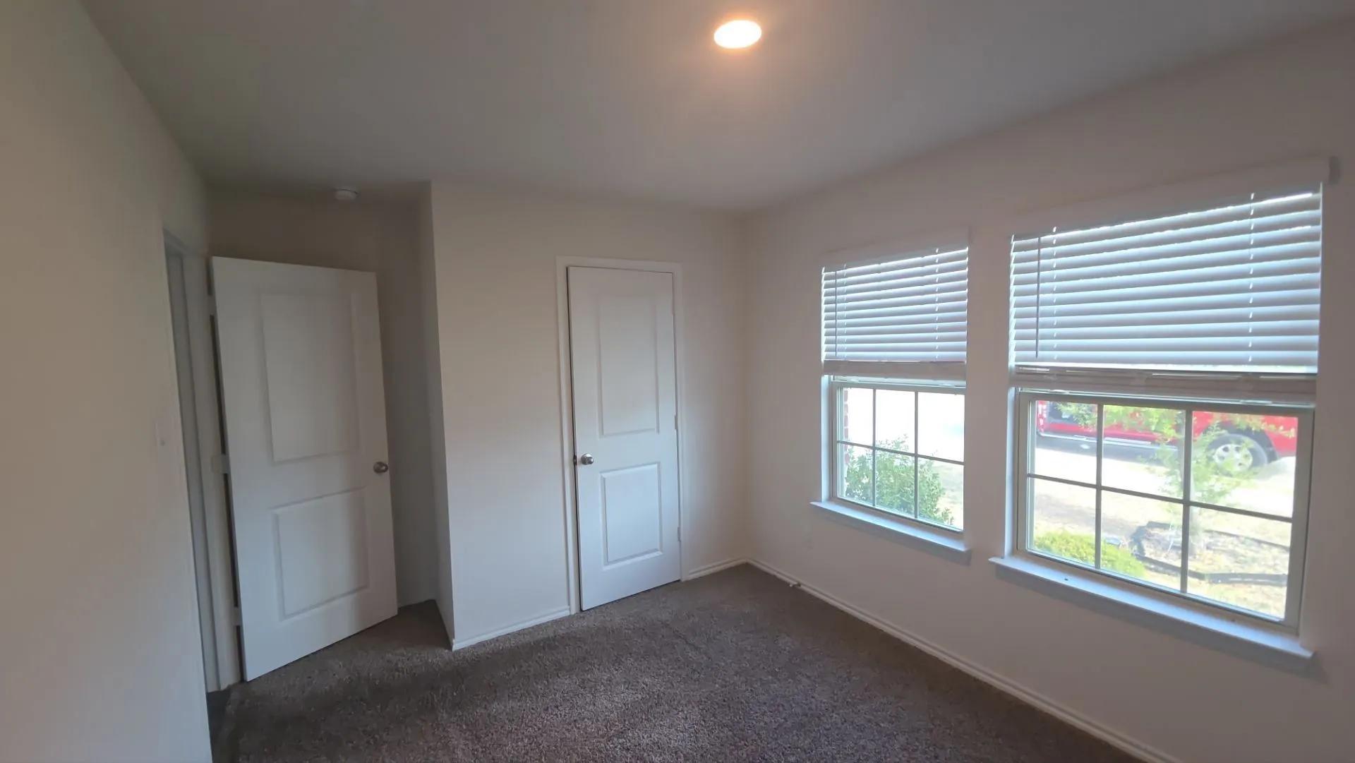 Recessed ceiling light, two windows with blinds, carpeted flooring, and two interior doors