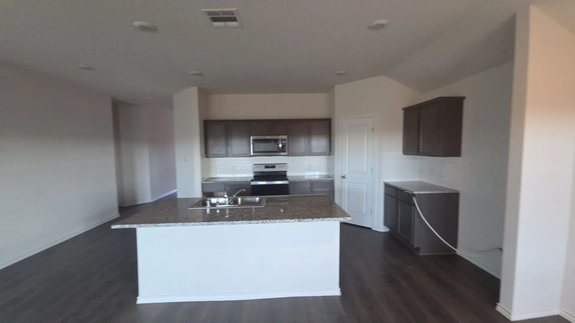 Kitchen featuring a central island with sink, wood-finish flooring, recessed lighting, and dark wood-finish cabinetry