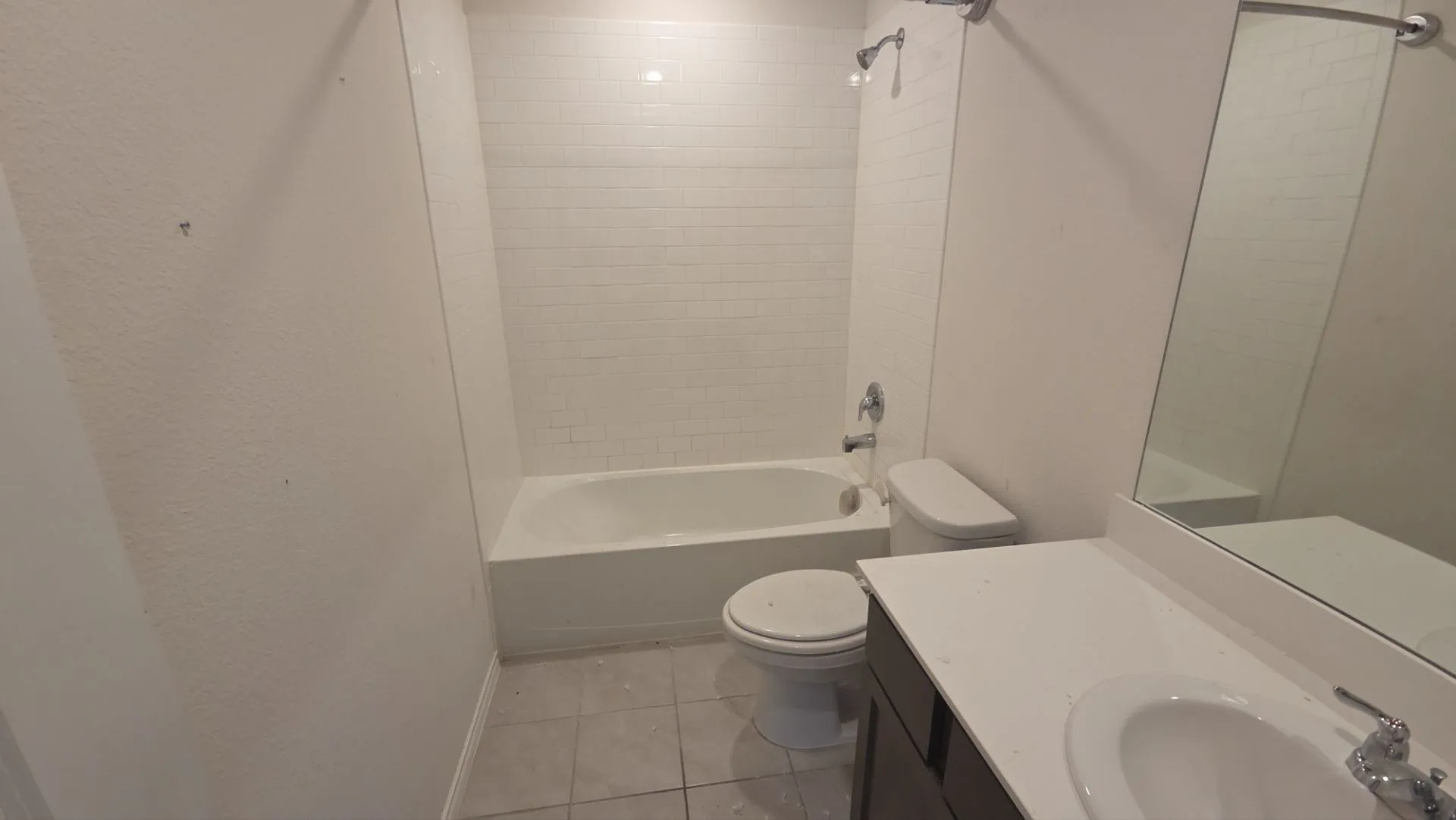 White subway tile shower surround with a built-in tub, single vanity with integrated sink, and a large wall mirror