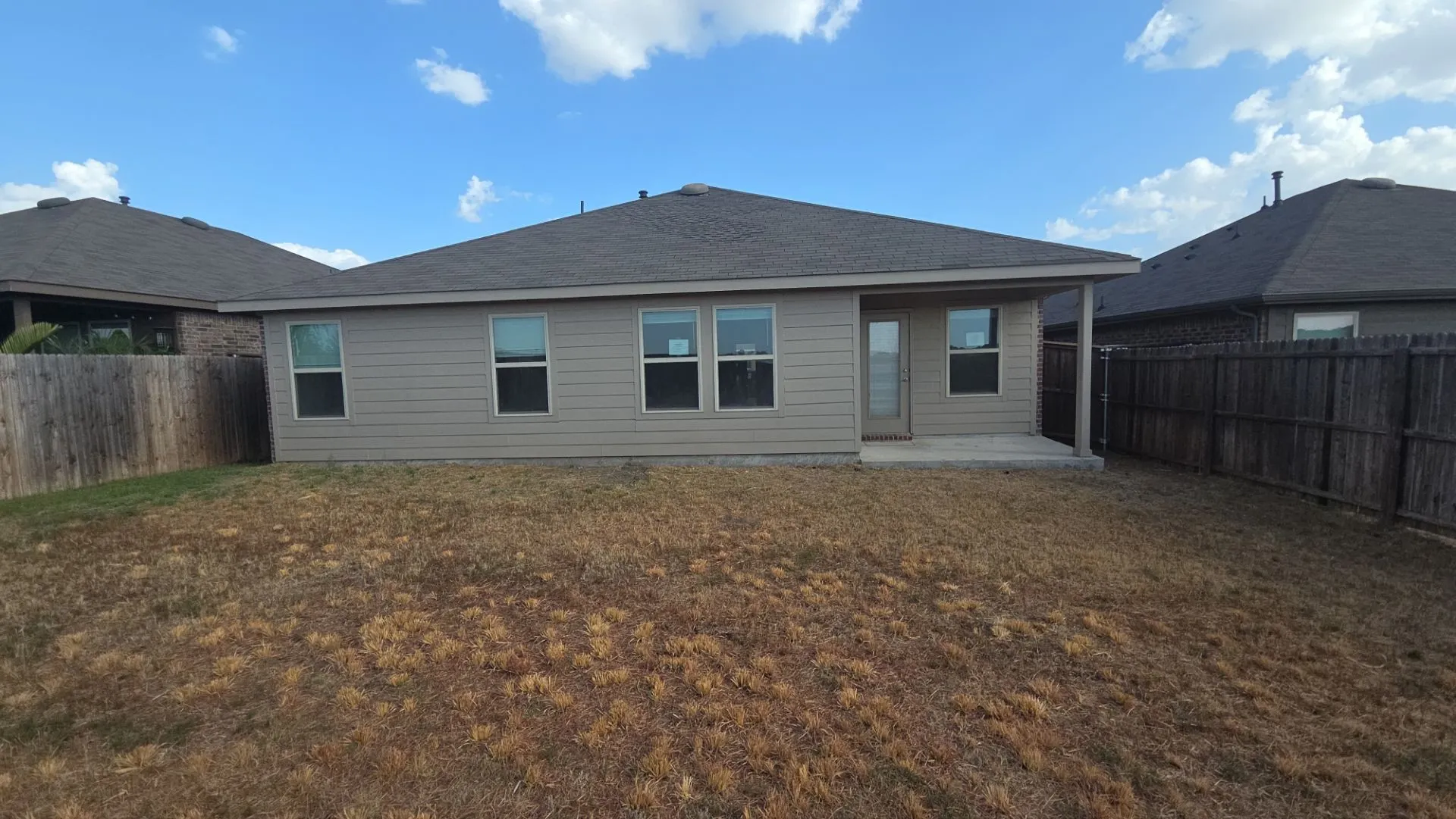 Rear elevation featuring horizontal siding, multiple windows, a covered patio, and a privacy fence