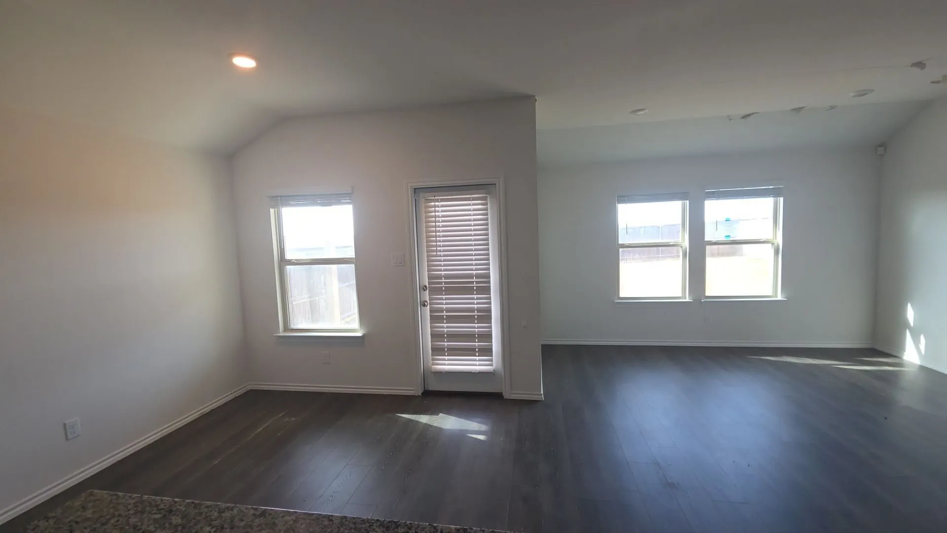Spacious interior featuring dark wood-finish flooring, multiple windows with natural light exposure, and recessed ceiling lighting