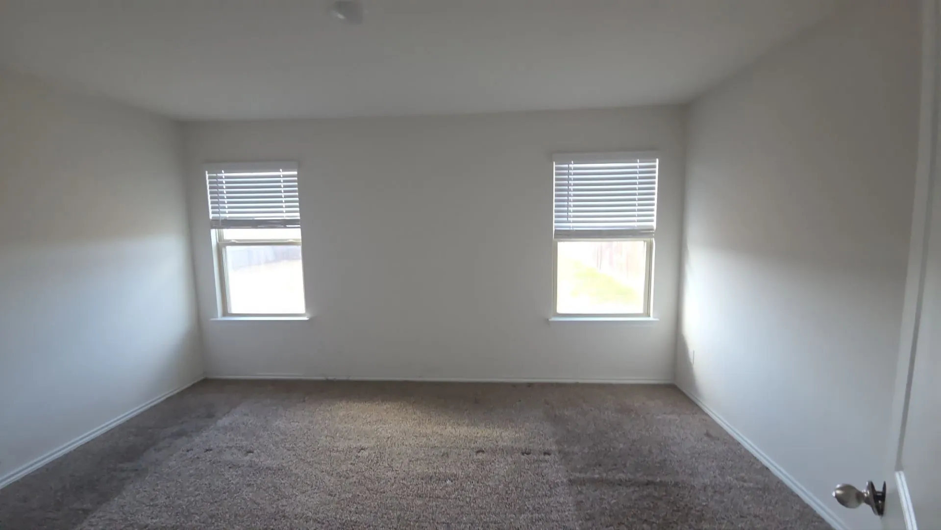 Neutral wall finishes with two windows featuring horizontal blinds