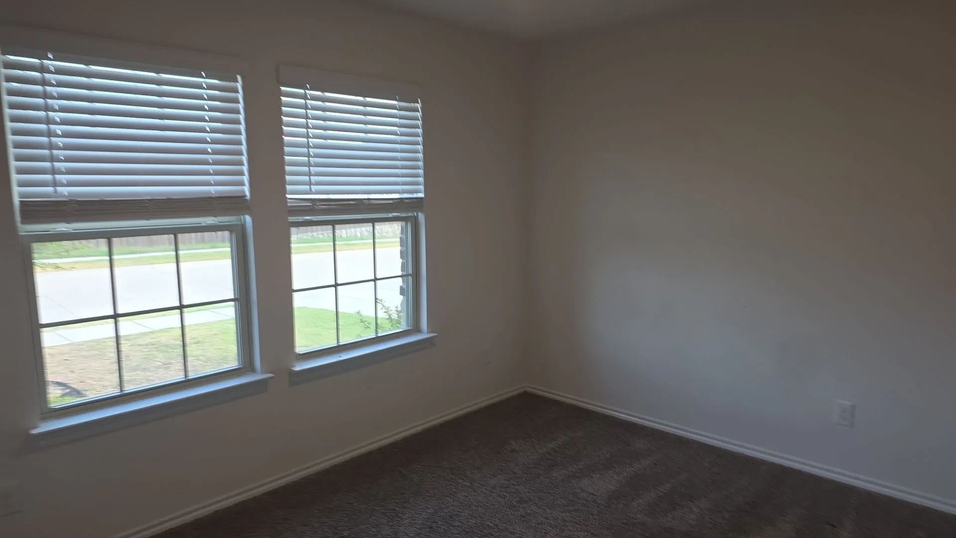 Two windows with white blinds, neutral wall paint, and gray carpeted flooring