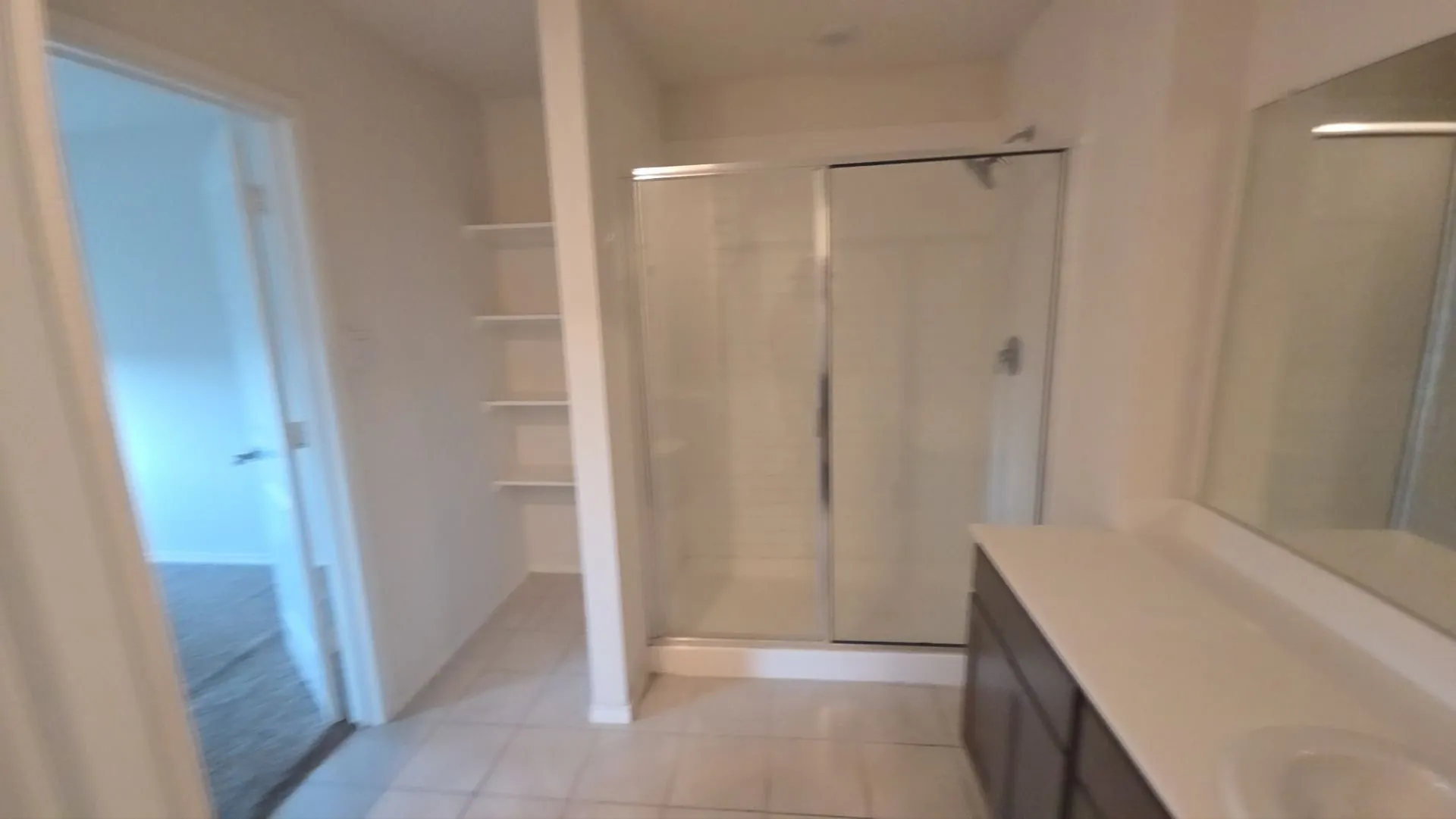 Tiled flooring, built-in shelving, glass-enclosed shower, vanity with an integrated sink, and a large wall-mounted mirror