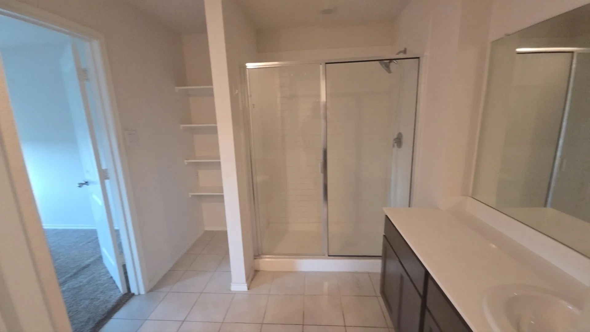 Glass-enclosed shower with a brushed nickel showerhead, a single vanity with an integrated sink, and an expansive wall mirror