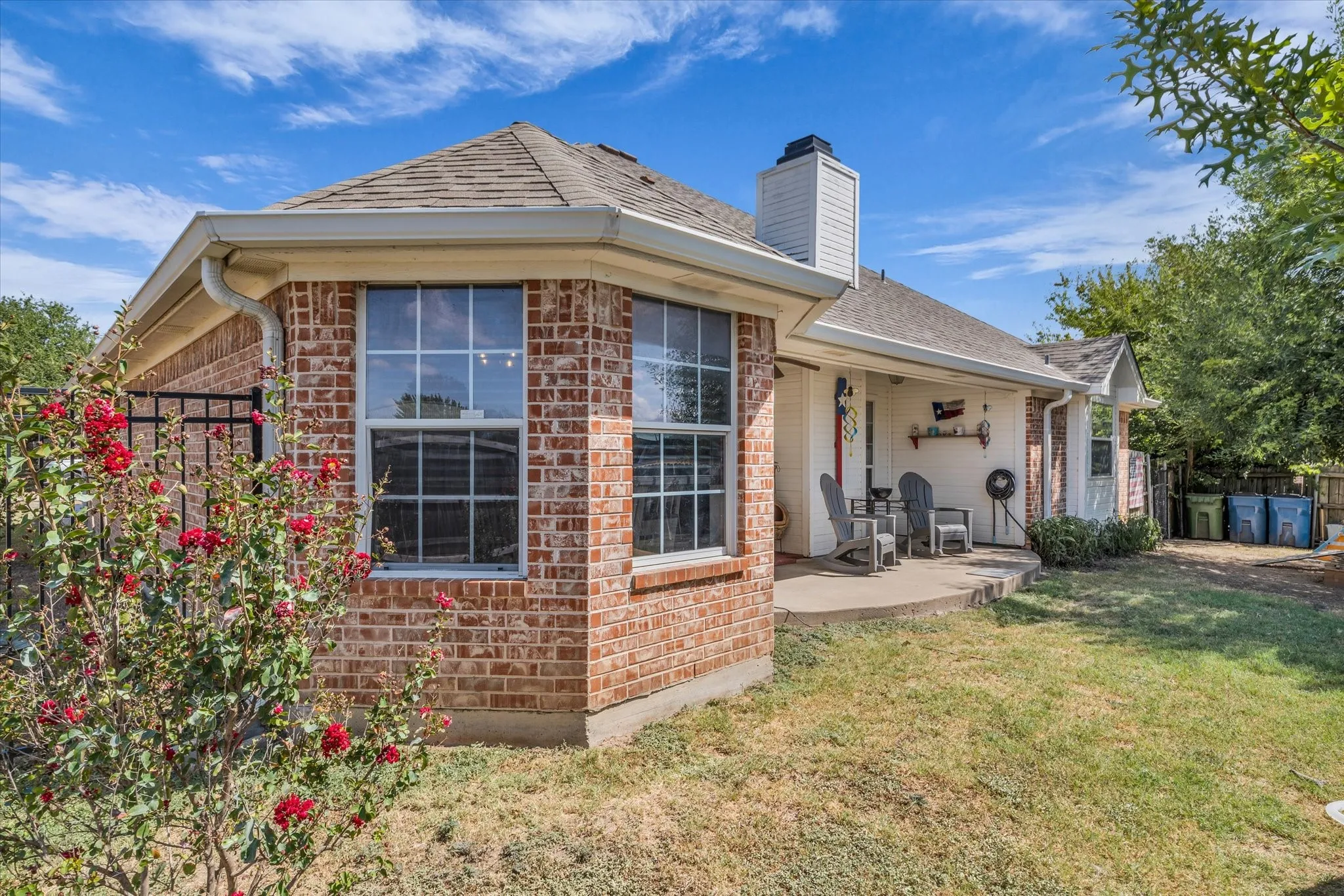 Brick exterior with a covered patio, gabled roof, and a fenced yard