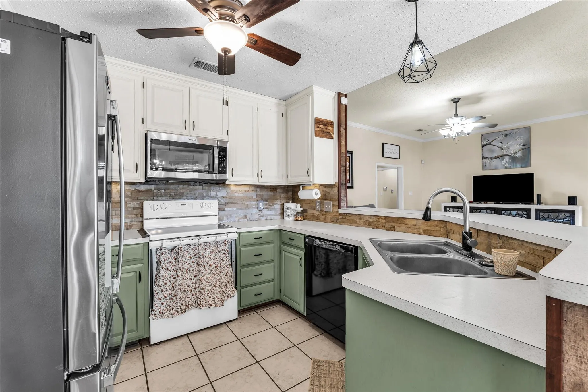 Kitchen featuring white and green cabinetry, stainless steel appliances, tiled backsplash, and a dual-basin sink with a gooseneck faucet