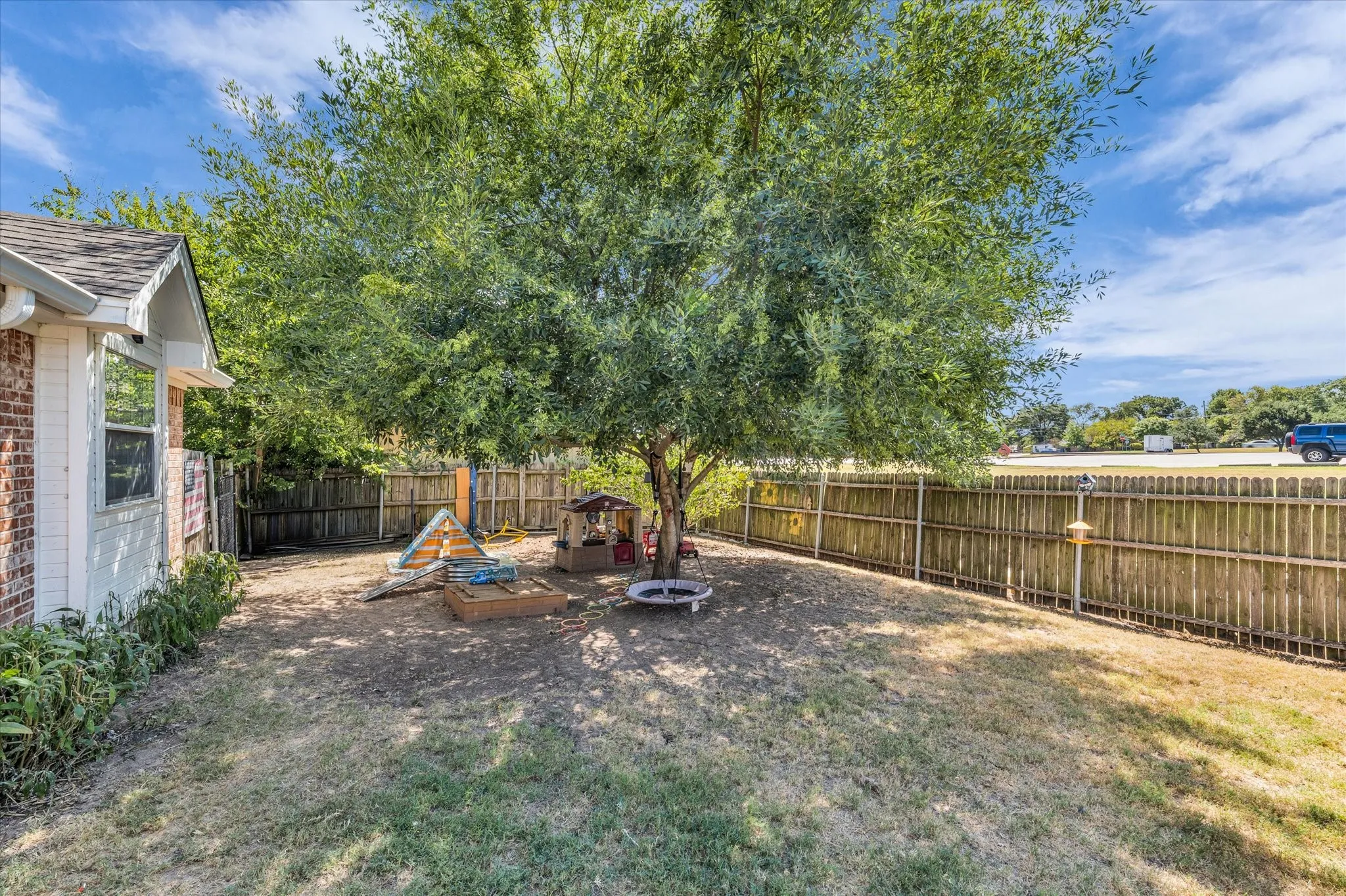 Expansive backyard featuring a mature tree, wood fencing, and a brick and siding exterior