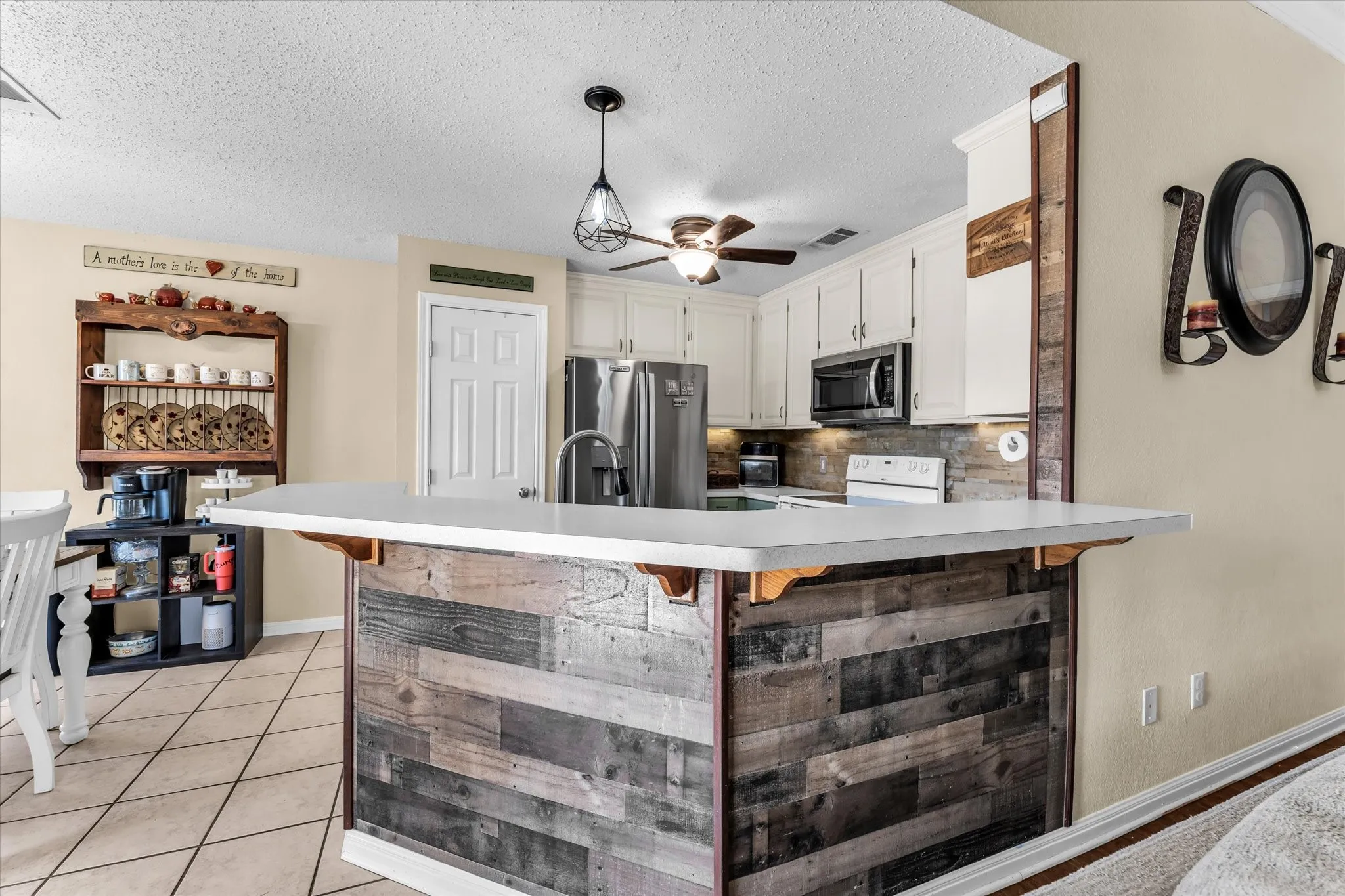 Kitchen featuring white cabinetry, stainless steel appliances, a breakfast bar with a wood-finish facade, and tile flooring
