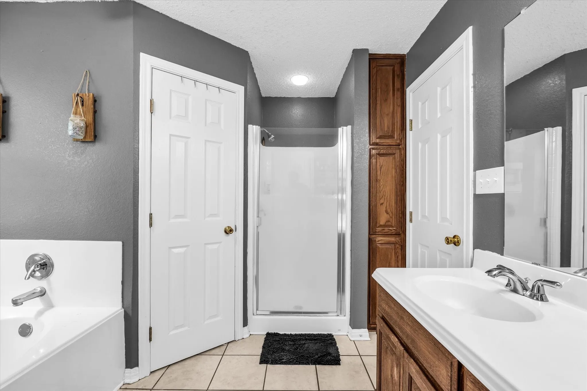White bathtub with chrome fixtures, tiled flooring, wood-finish vanity with white countertop, recessed lighting, and a walk-in shower with a glass enclosure