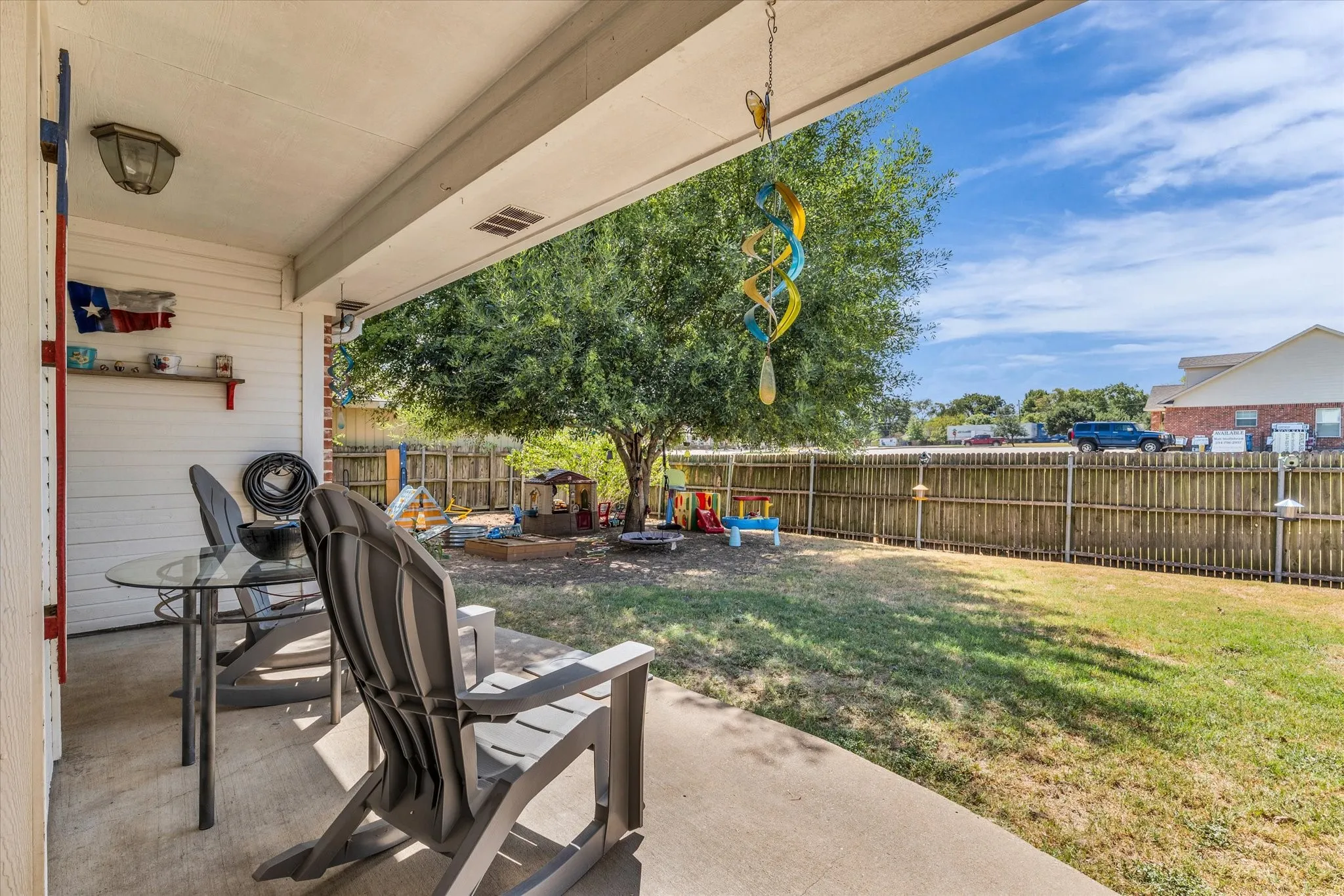Covered concrete patio with overhead lighting, featuring a privacy fence and mature tree