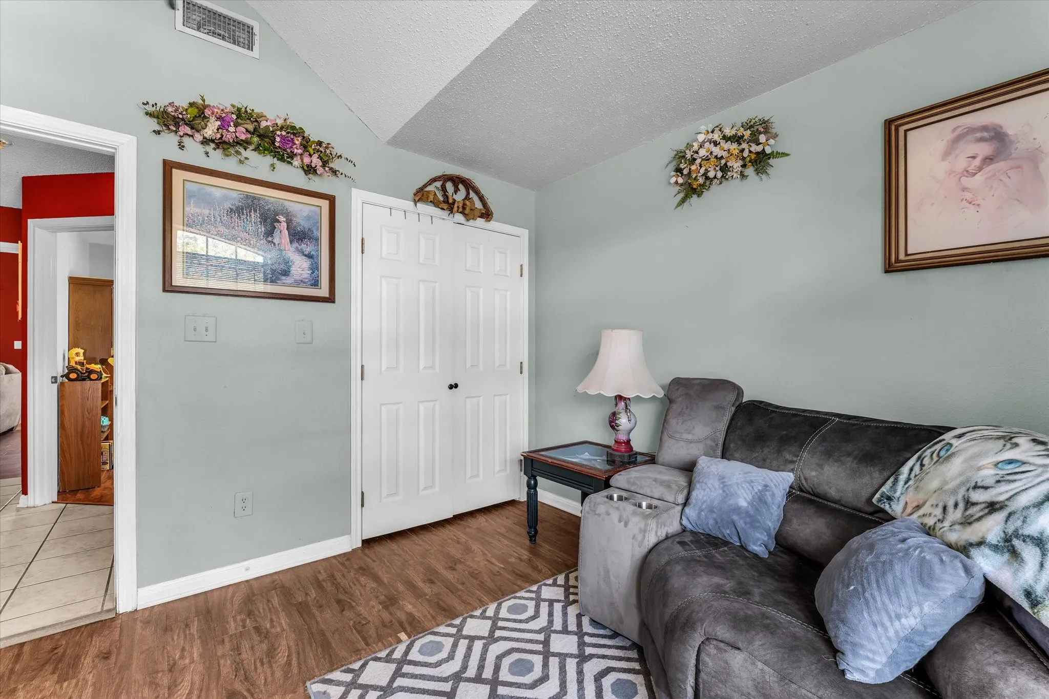 Vaulted ceiling, wood-finish flooring, white bi-fold closet doors, wall-mounted air vent, light-colored wall paint