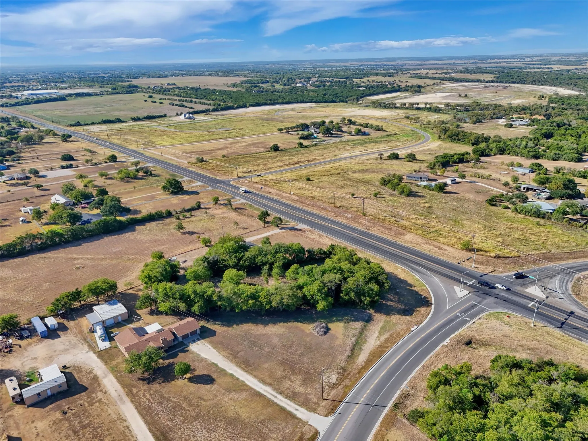 Expansive land parcel featuring direct road frontage, multiple existing structures, mature trees, and a clear, level topography