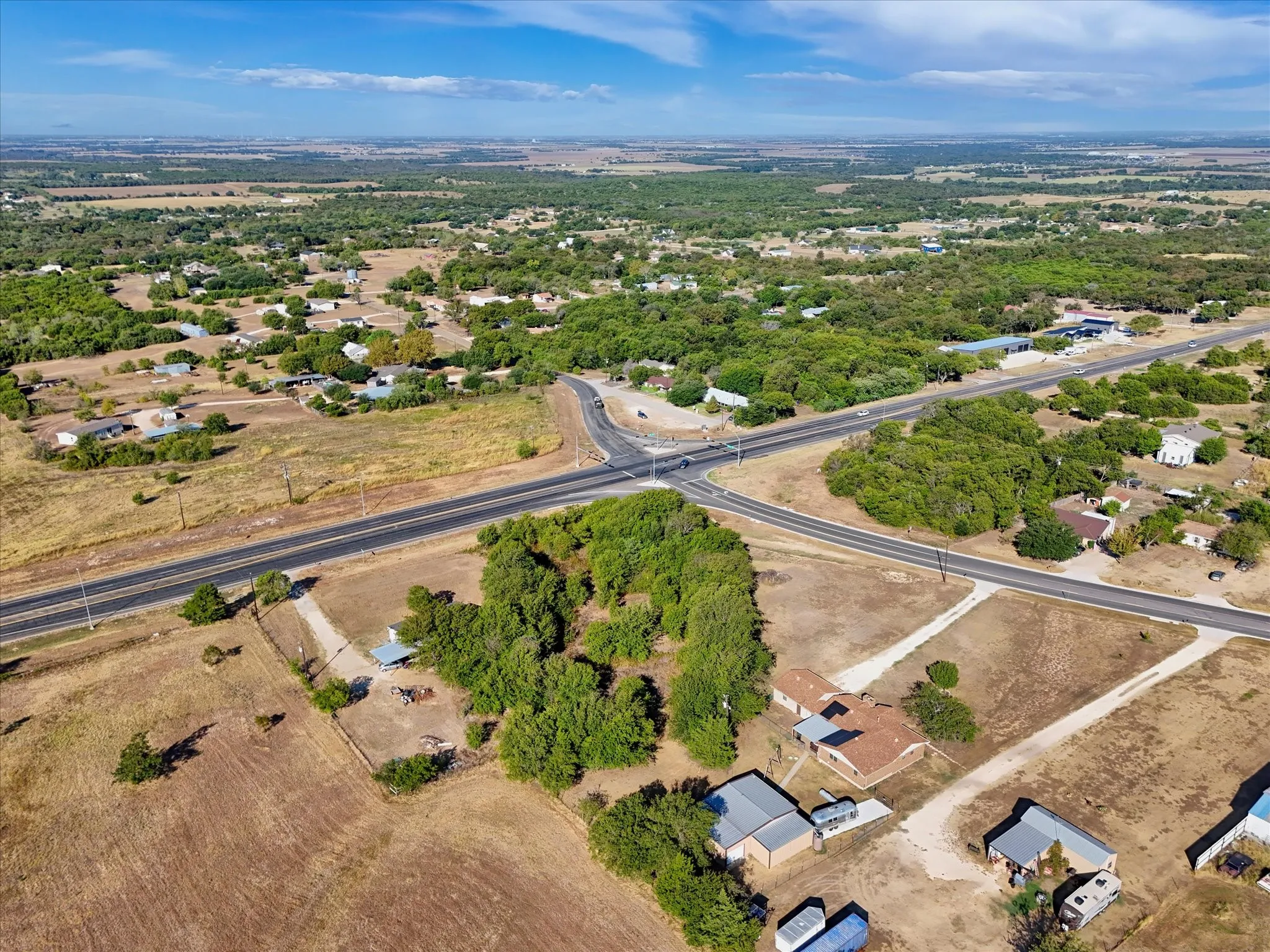 Expansive land featuring a road intersection, scattered residential structures, and abundant natural foliage