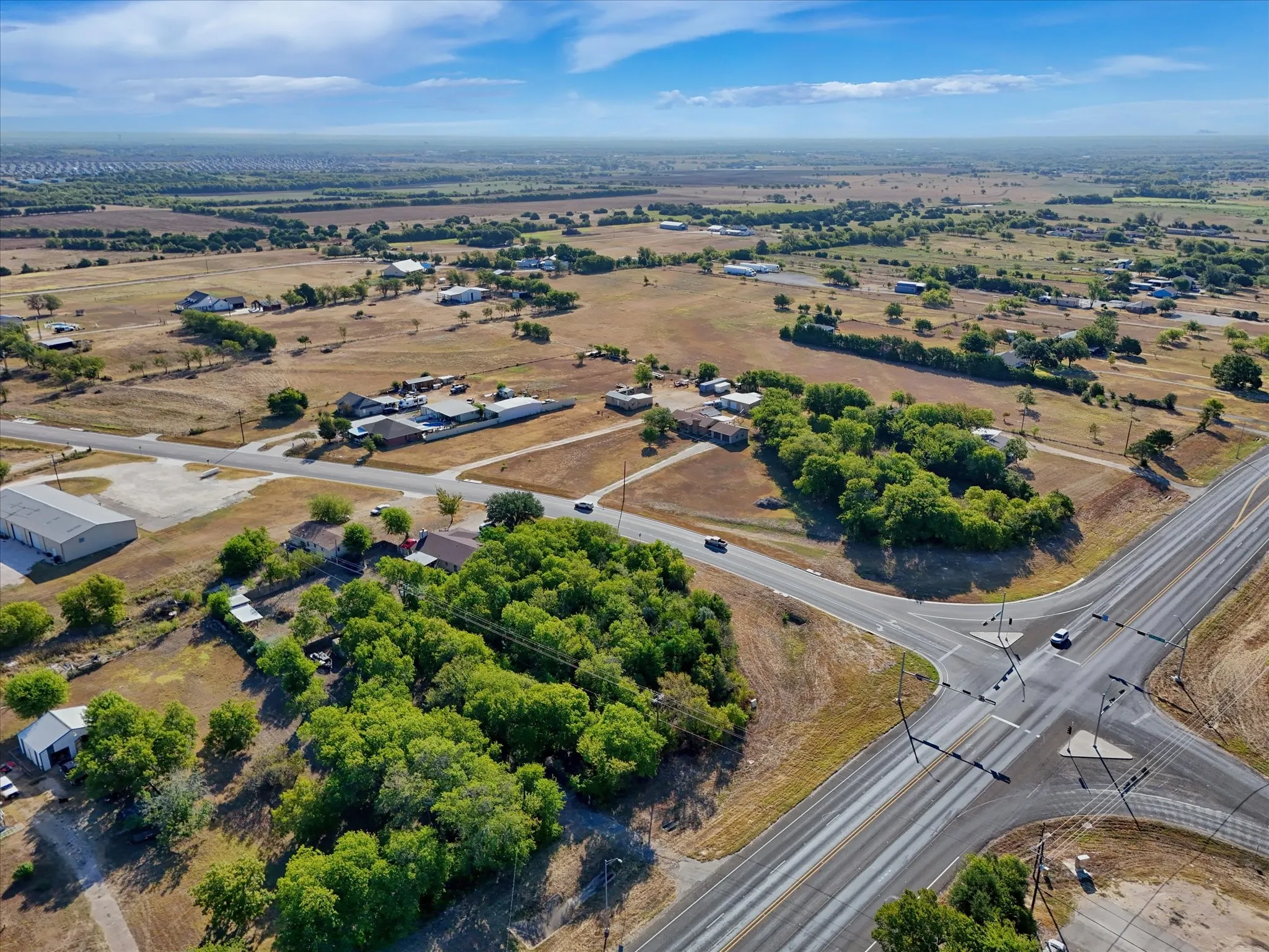 Expansive rural landscape featuring scattered residential structures, mature trees, and an intersecting highway