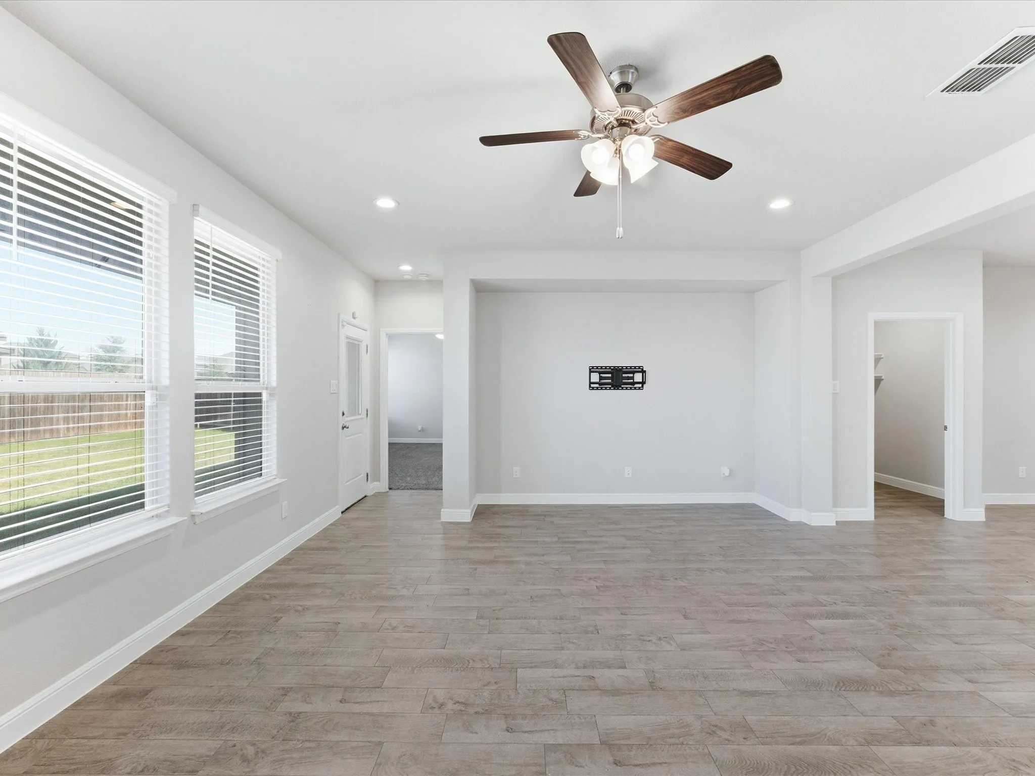 Spacious room featuring wood-finish flooring, multiple windows with blinds, a ceiling fan with integrated lighting, and recessed lighting