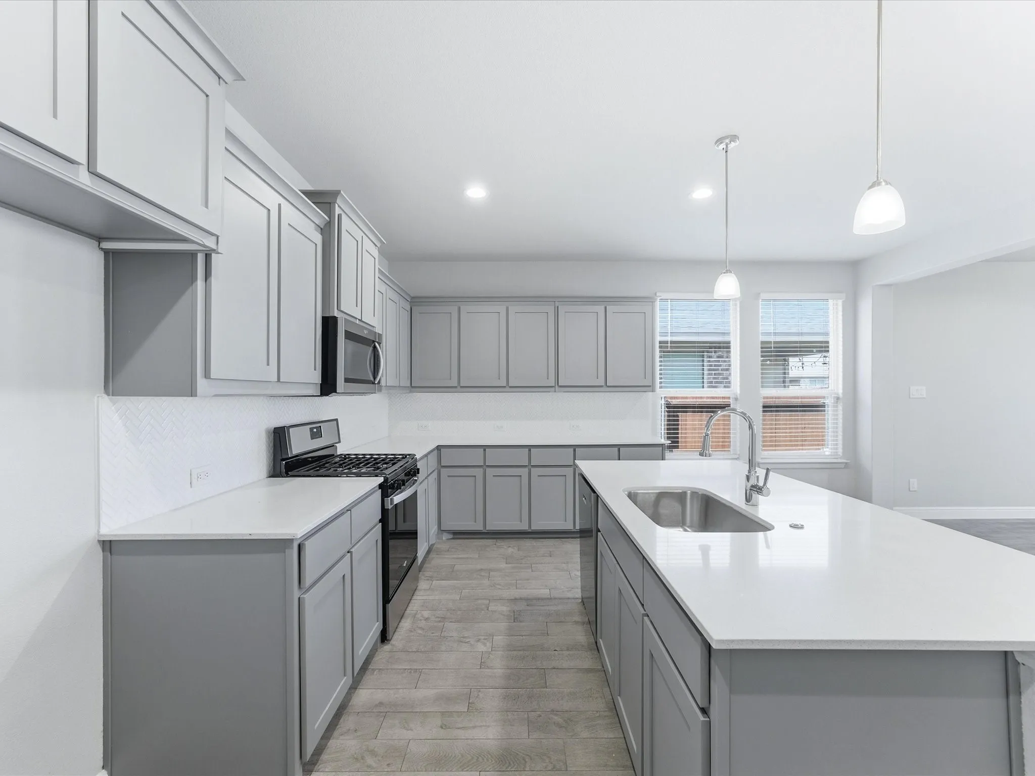 Kitchen featuring gray shaker cabinetry, white countertops, a chevron pattern tile backsplash, a stainless steel sink, and stainless steel appliances