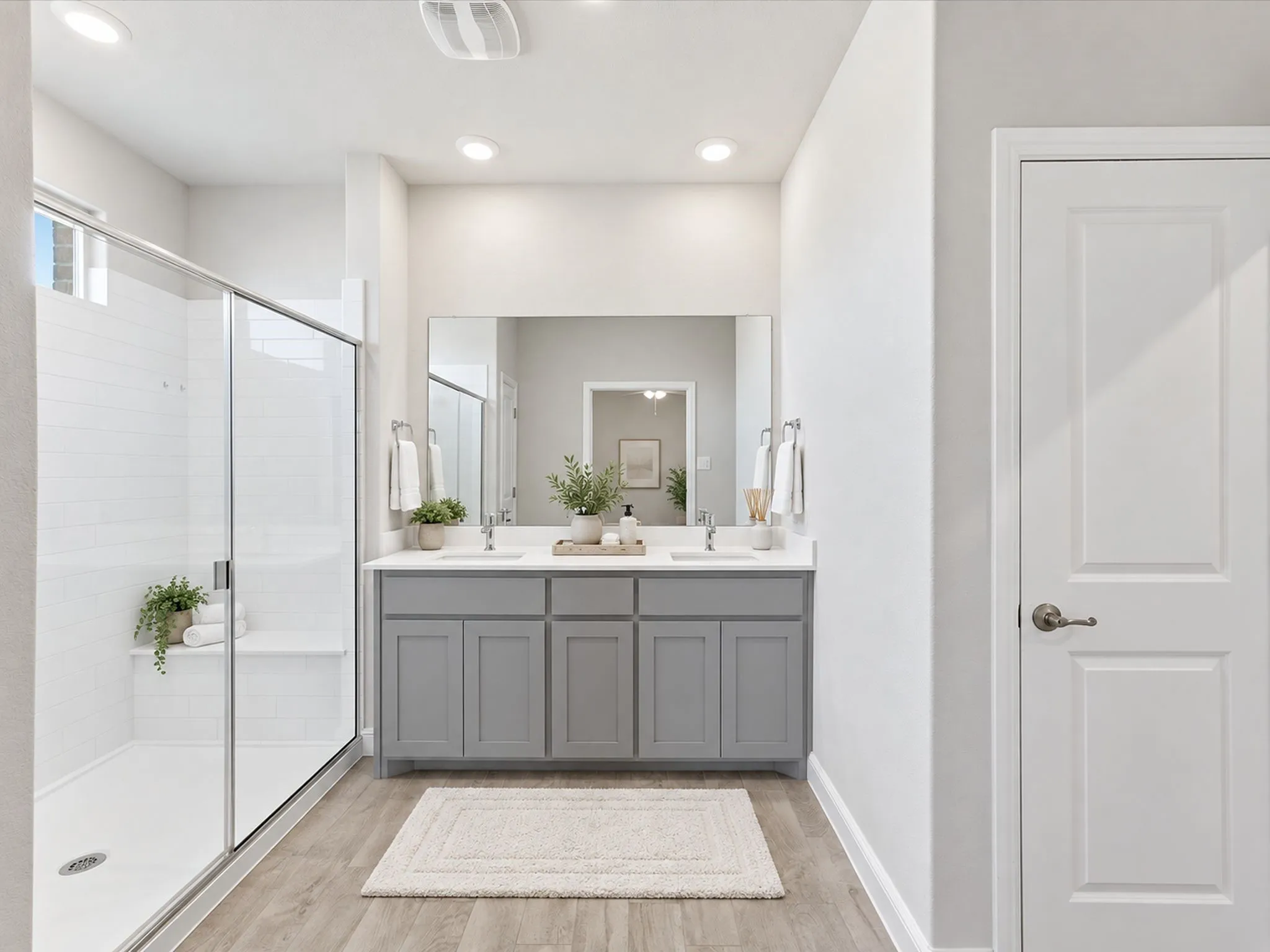 Dual sink vanity with grey cabinetry, rectangular mirror, wood-finish flooring, glass-enclosed shower, and white subway tile surround