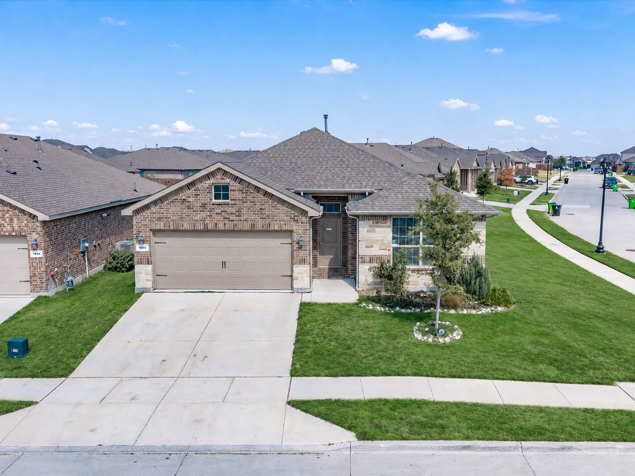 Brick and stone exterior with an attached garage, concrete driveway, and a shingled roof