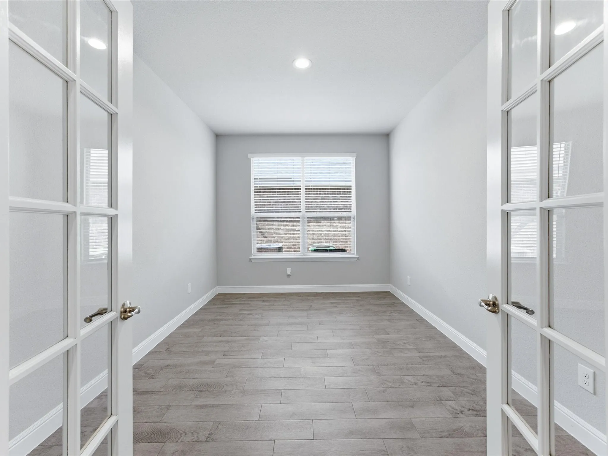 Recessed lighting illuminates the room, featuring wood-finish flooring and a window with blinds