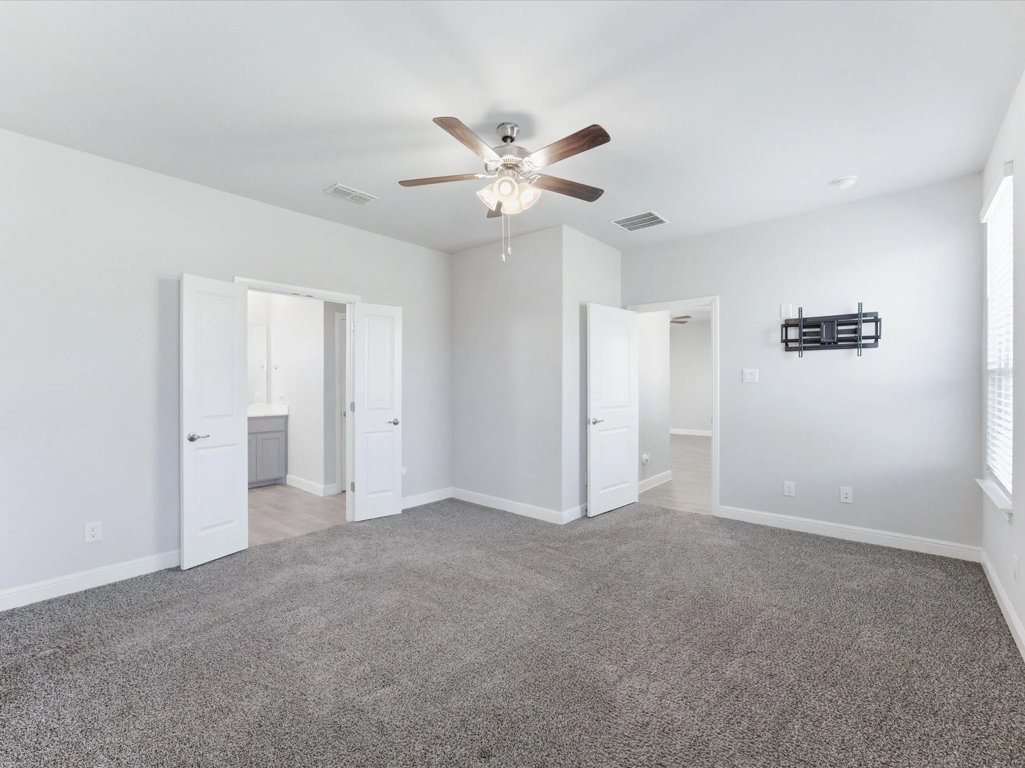 Spacious room featuring gray carpeting, a ceiling fan with integrated lighting, white walls, and white plantation shutters