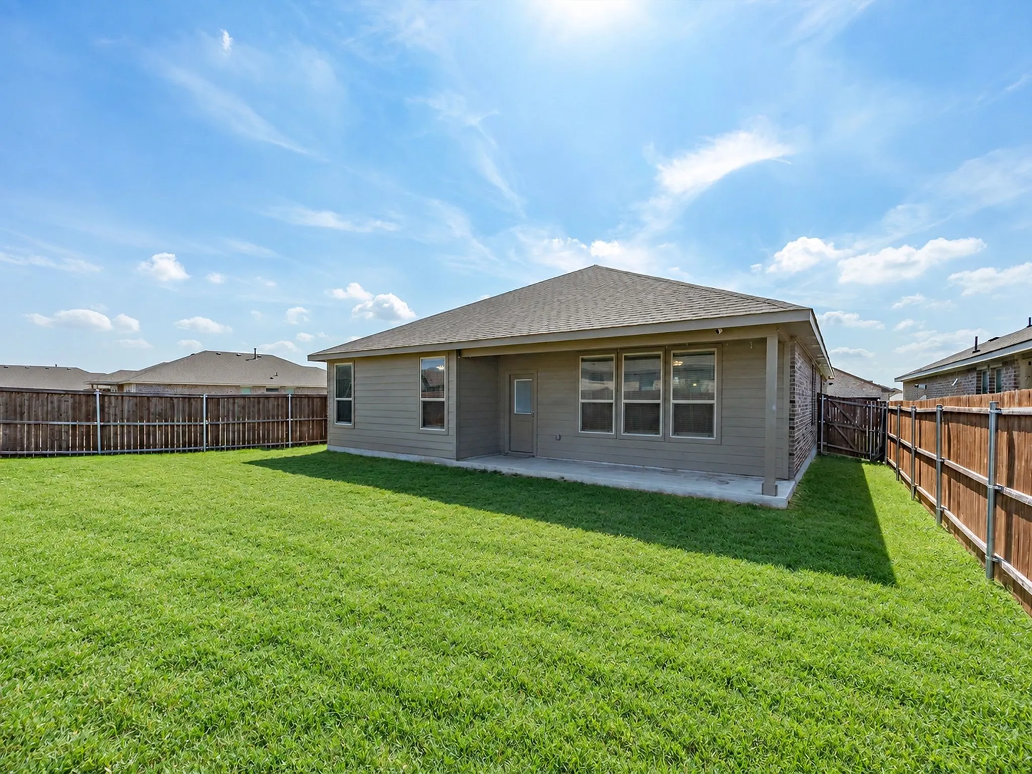 Expansive green lawn with a wood privacy fence, concrete patio, and a single-story residence featuring multiple windows