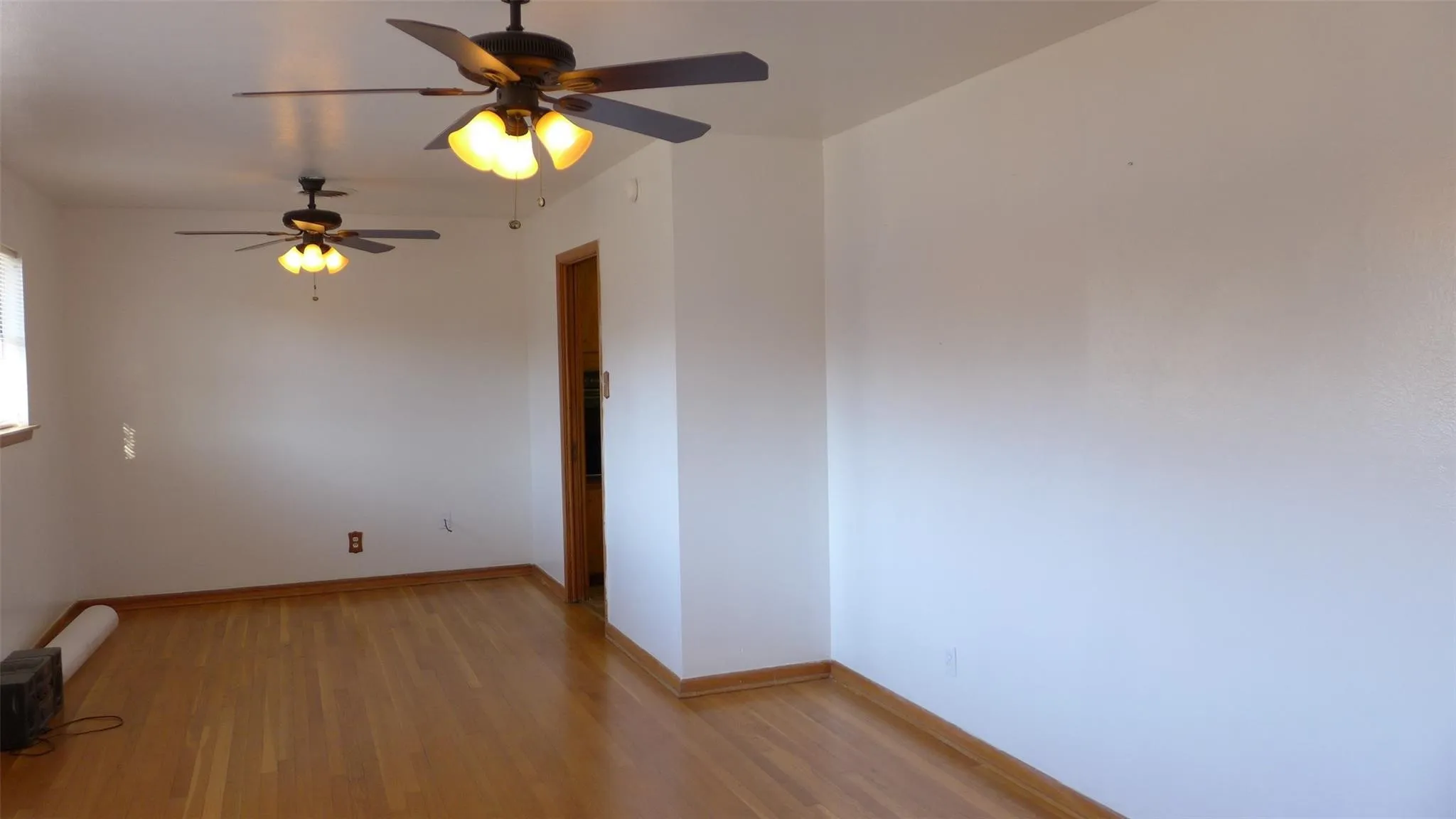 Hardwood flooring, painted white walls, two ceiling fans with light kits, and a wood-trim doorway