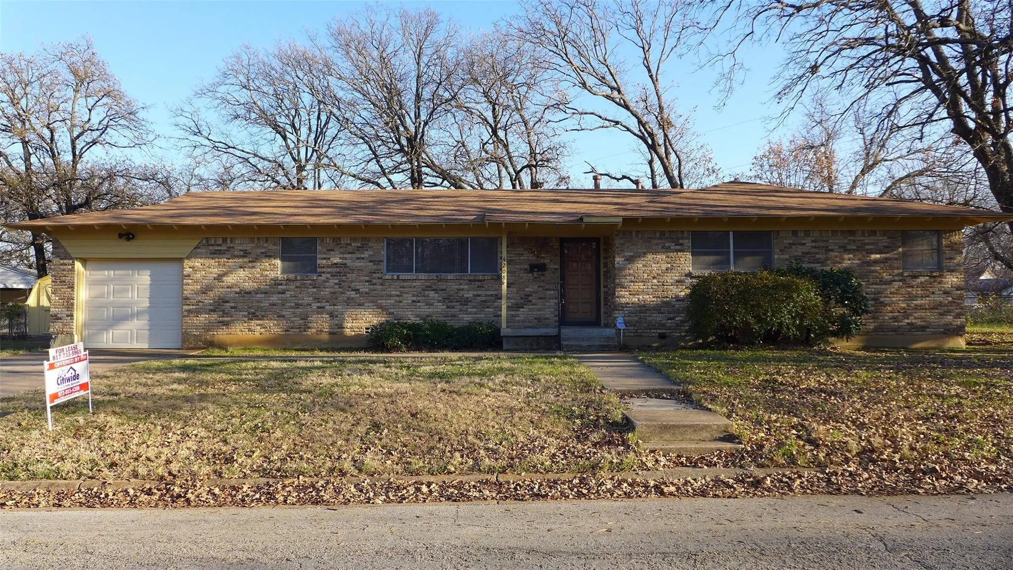 Brick exterior with an attached garage, covered entry, and mature trees