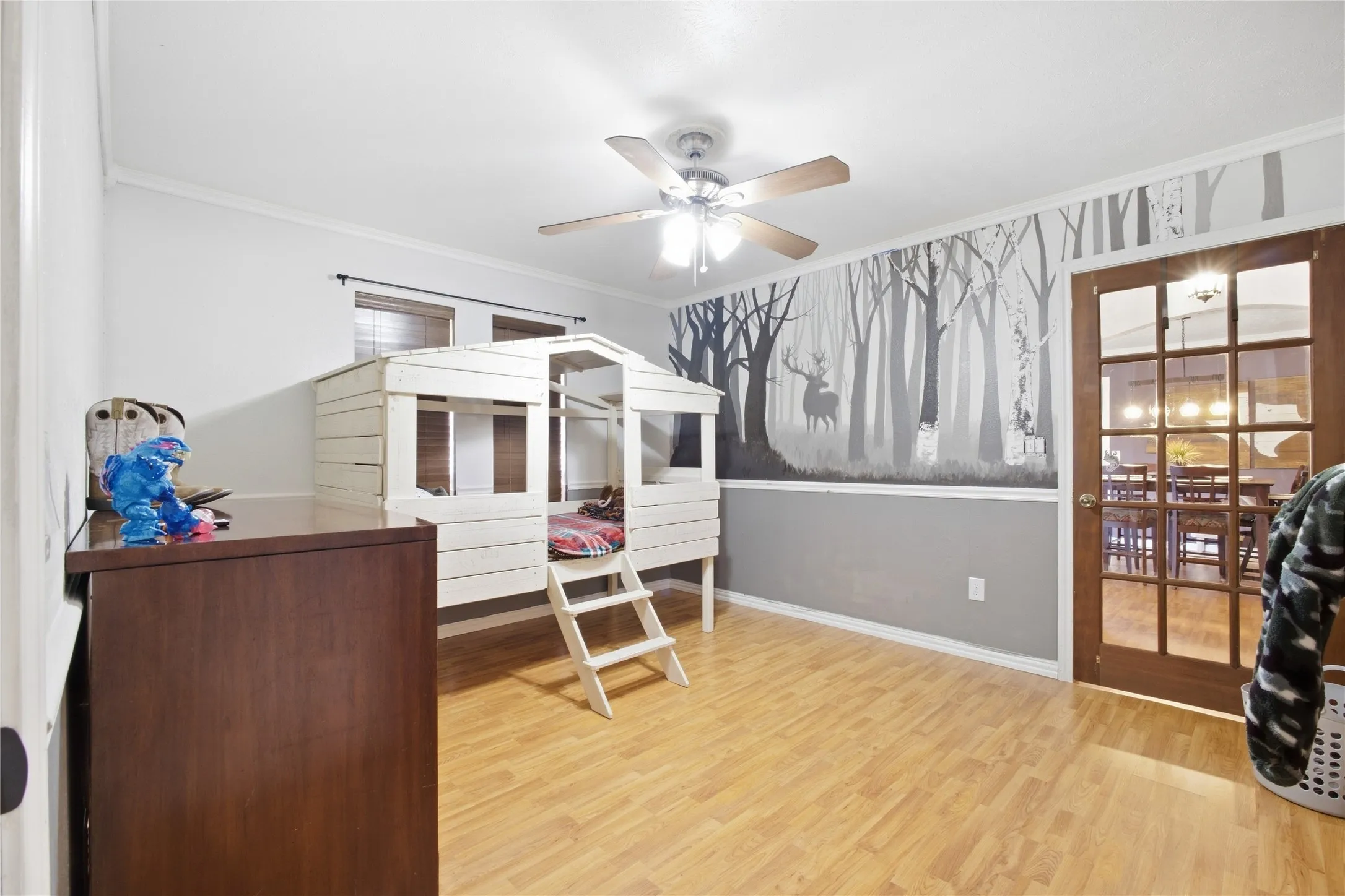 Wood-finish flooring, ceiling fan with light fixture, interior French door, crown molding, and a two-tone wall treatment