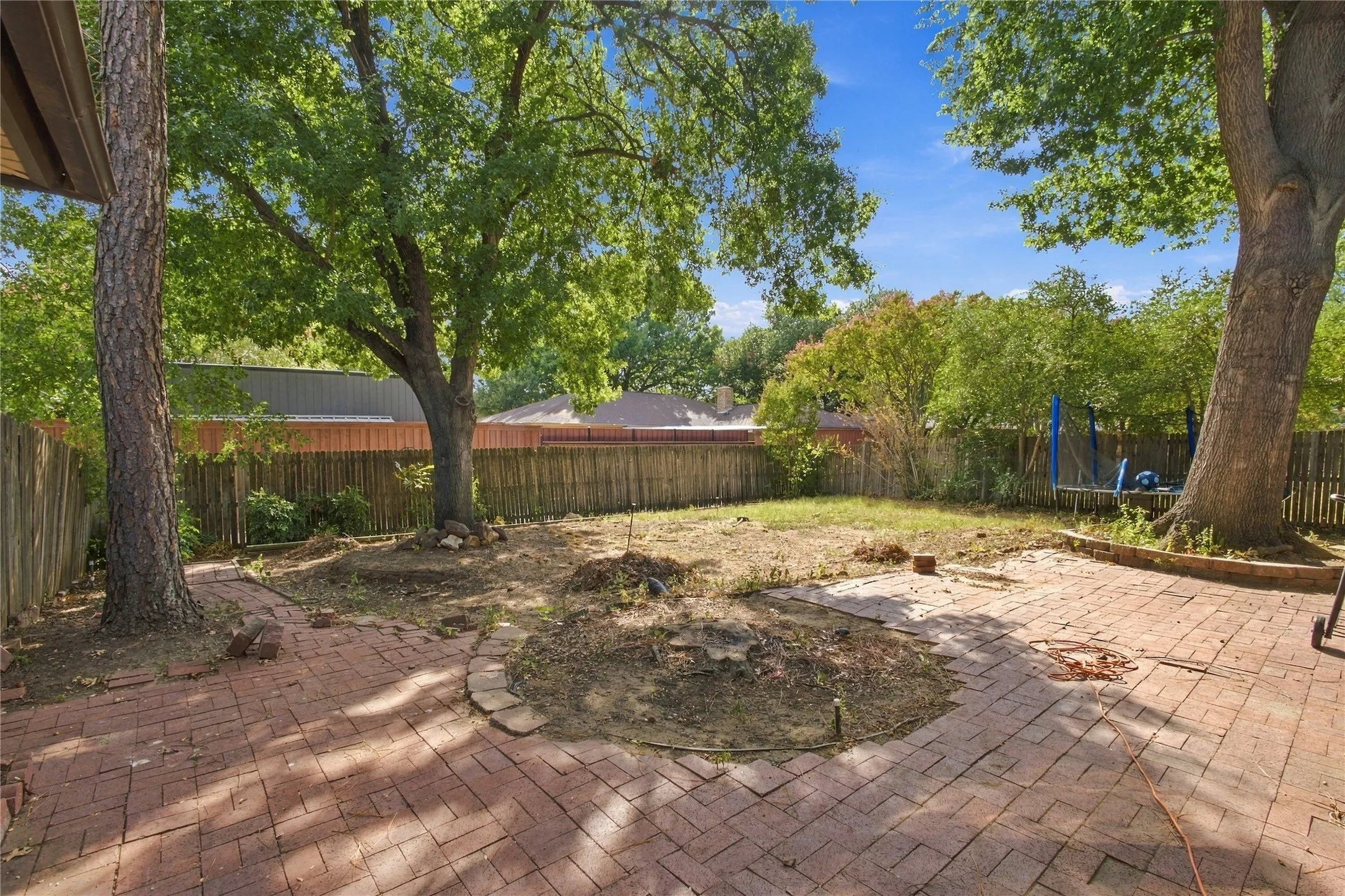 Expansive backyard featuring a brick paver patio, a circular brick-lined garden bed, and mature trees