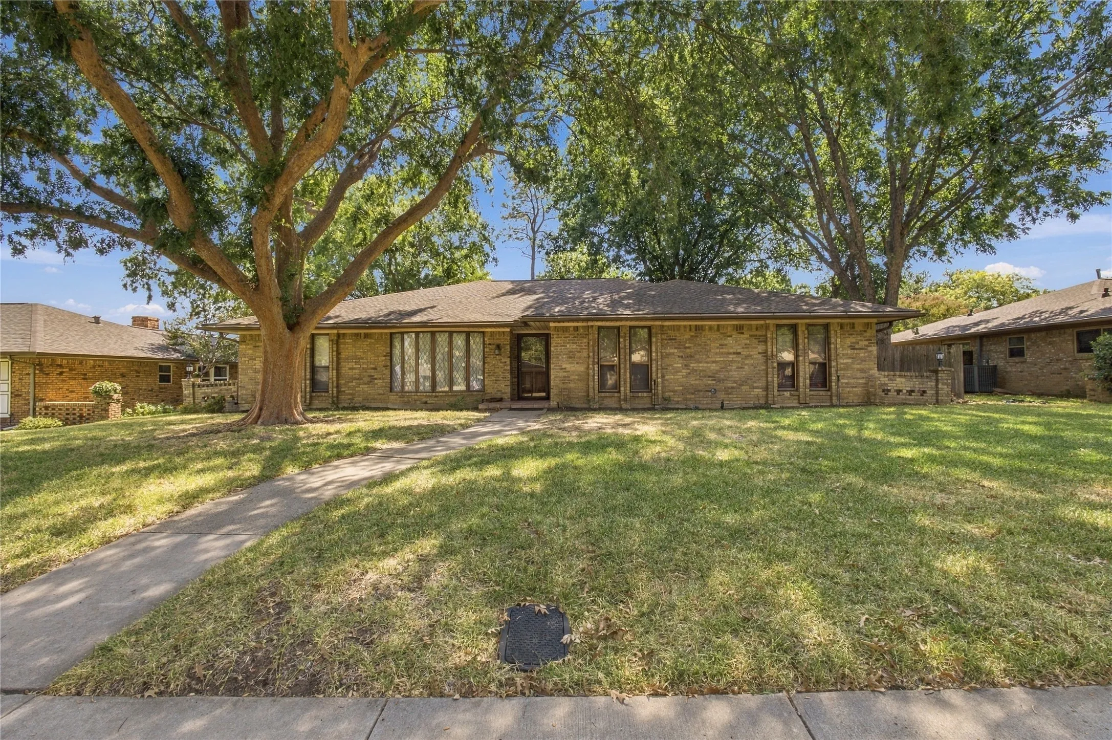 Stone-clad exterior, full front lawn, mature trees, concrete walkway, and a prominent front door