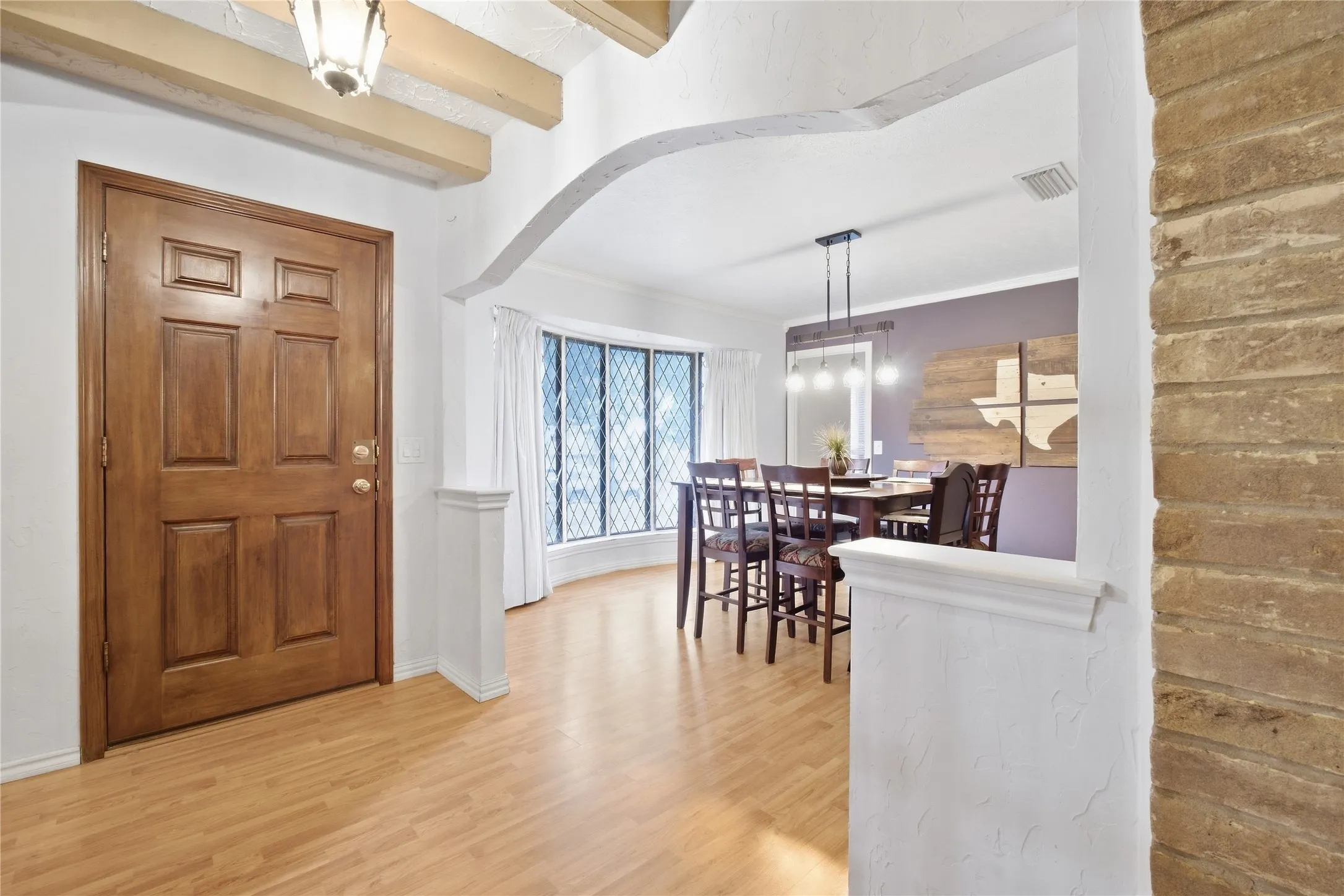 Wood-finish flooring, exposed ceiling beams, an arched entryway, and a bay window with decorative grilles
