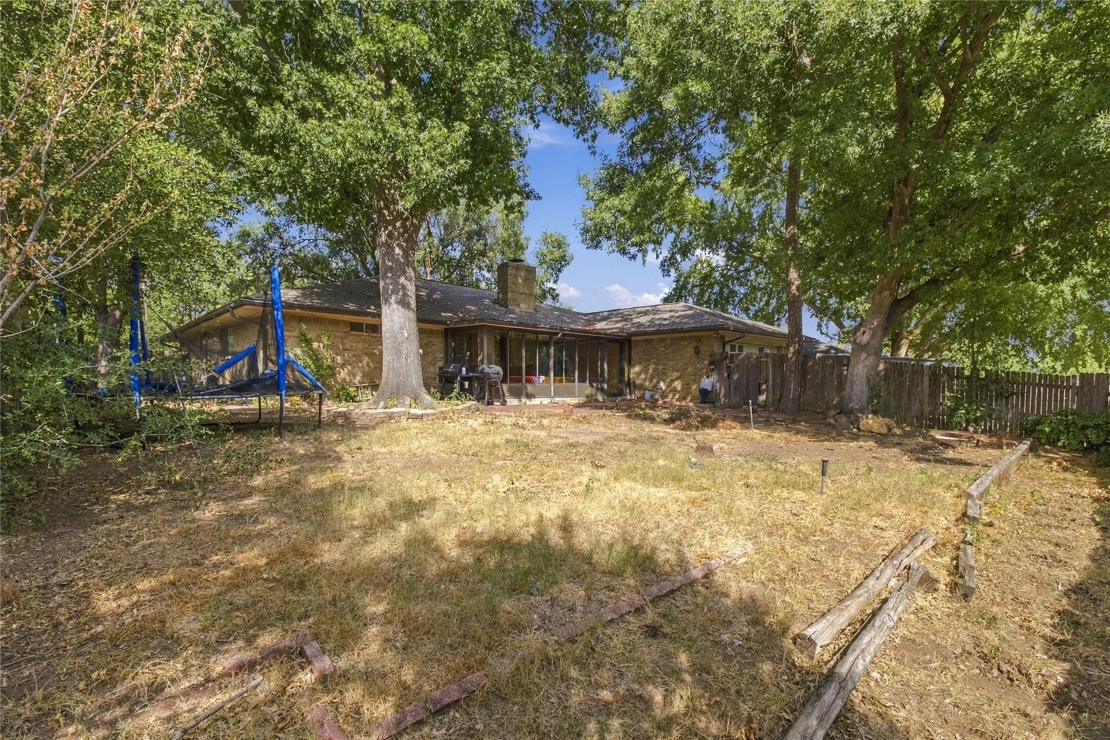 Expansive backyard featuring mature trees, a wood privacy fence, and an exterior brick finish
