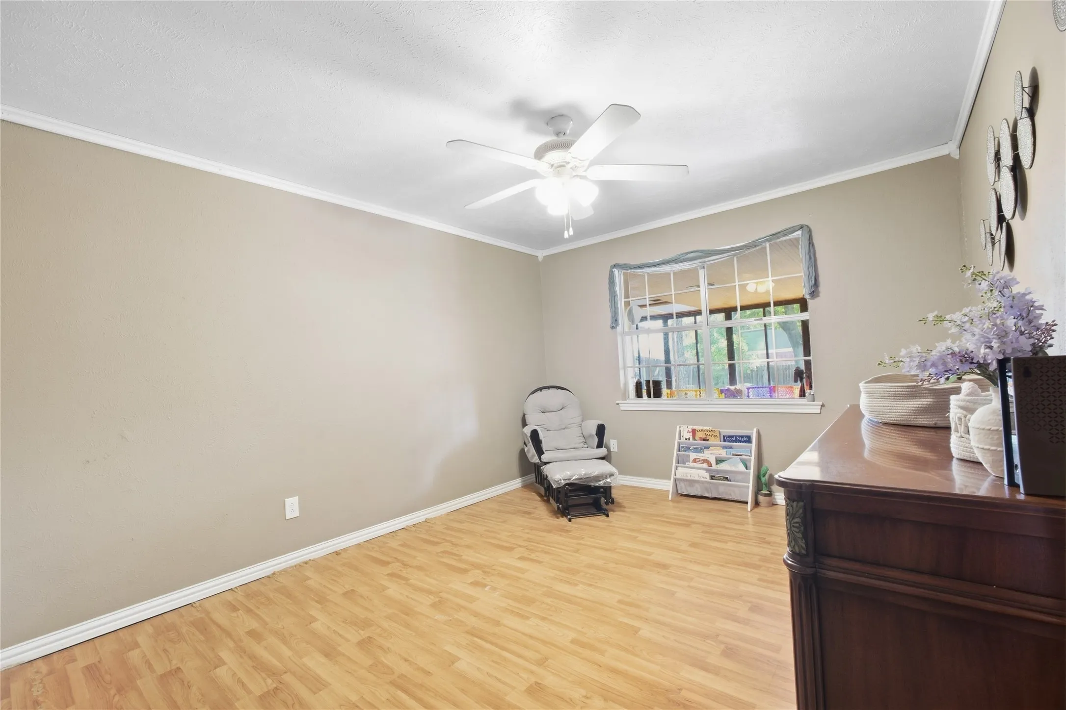 Wood-finish flooring with neutral wall paint, crown molding, and a ceiling fan with integrated lighting
