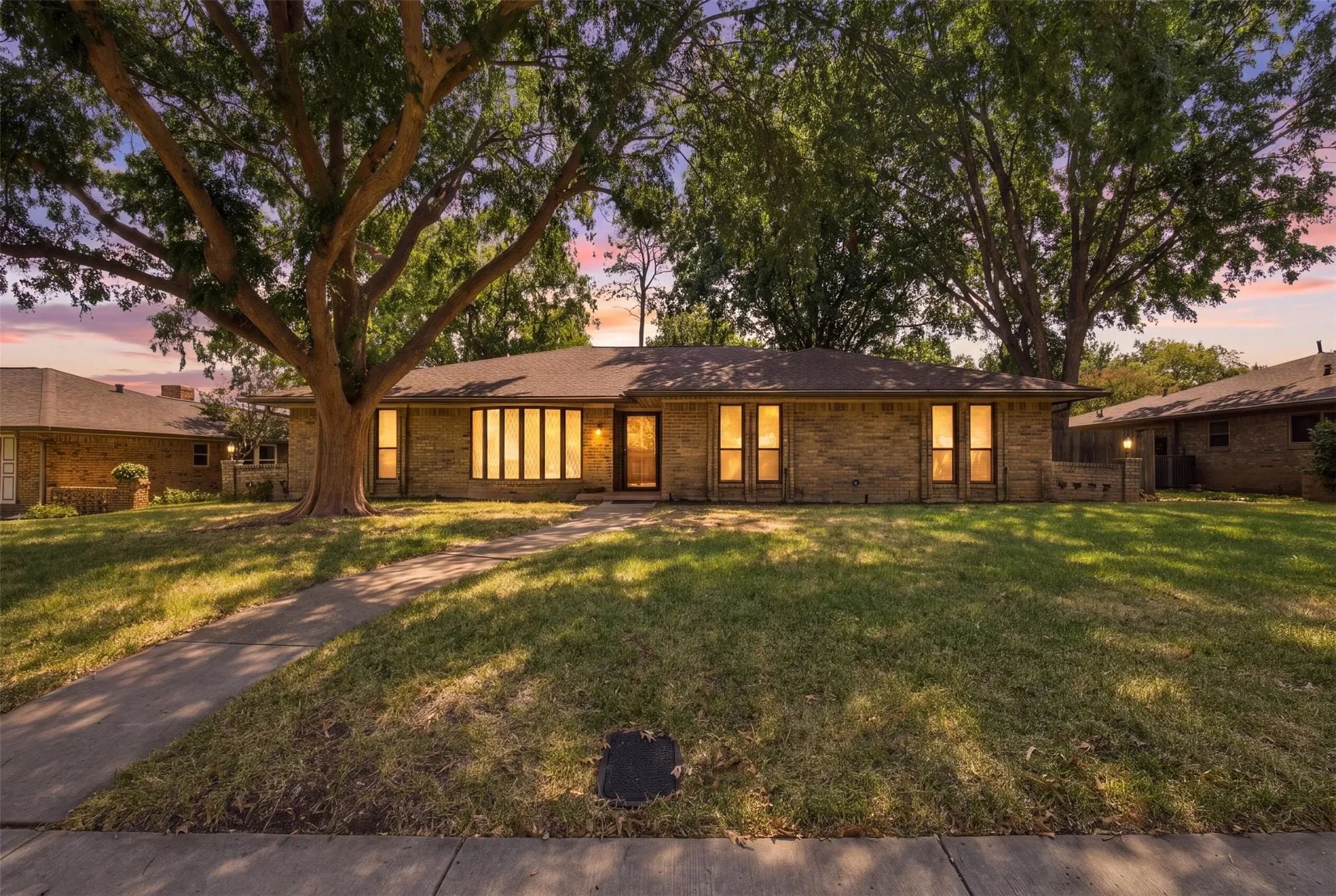 Brick exterior, large front yard, mature trees, concrete walkway, multiple windows
