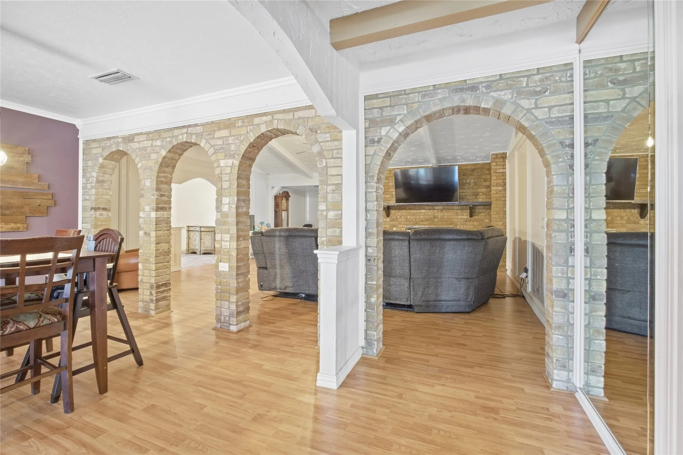 Wood-finish flooring throughout, multiple brick archways, recessed lighting, and mirrored closet doors