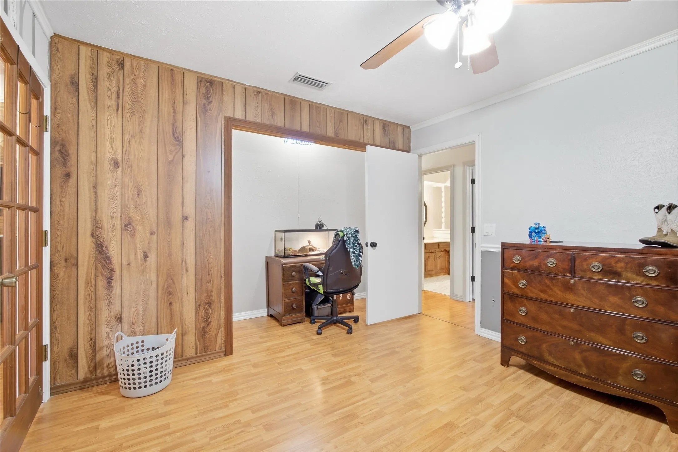 Wood paneling accent wall, wood-finish flooring, ceiling fan, and white trim