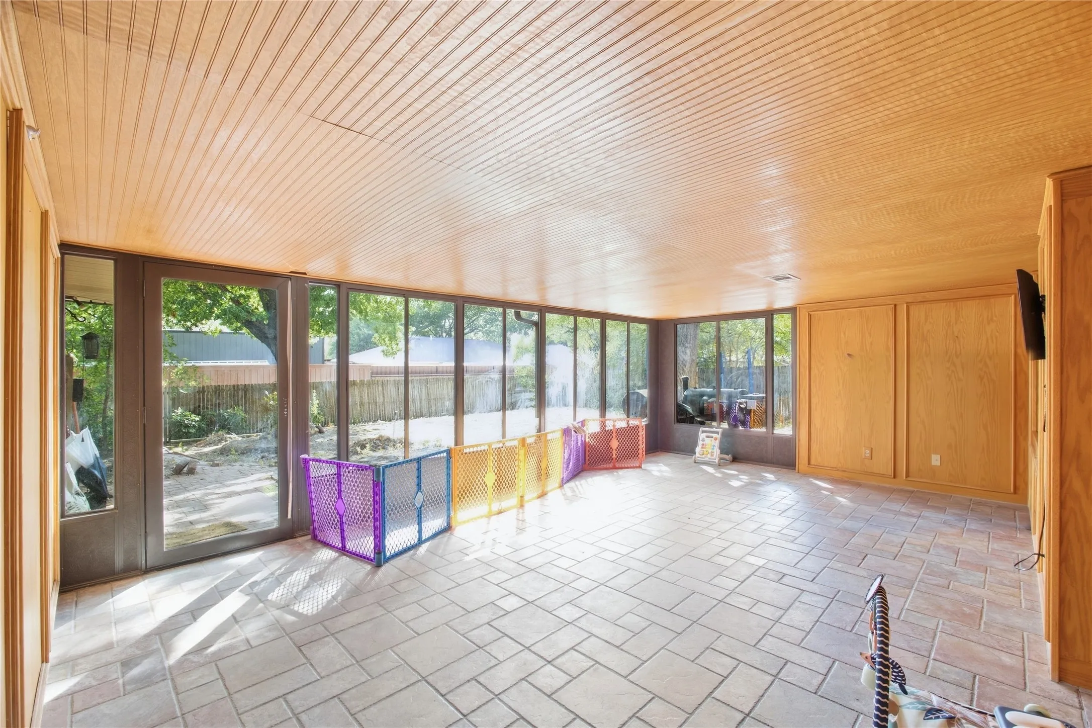 Expansive room featuring a wood-paneled ceiling, full-height windows, a glass door, and tiled flooring
