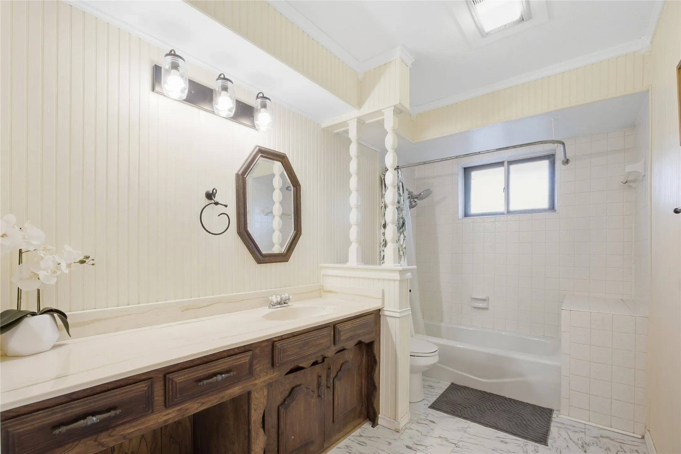 Bathroom featuring a wood-finish vanity with a light-colored countertop, beadboard wall paneling, and a bathtub with white tile surround